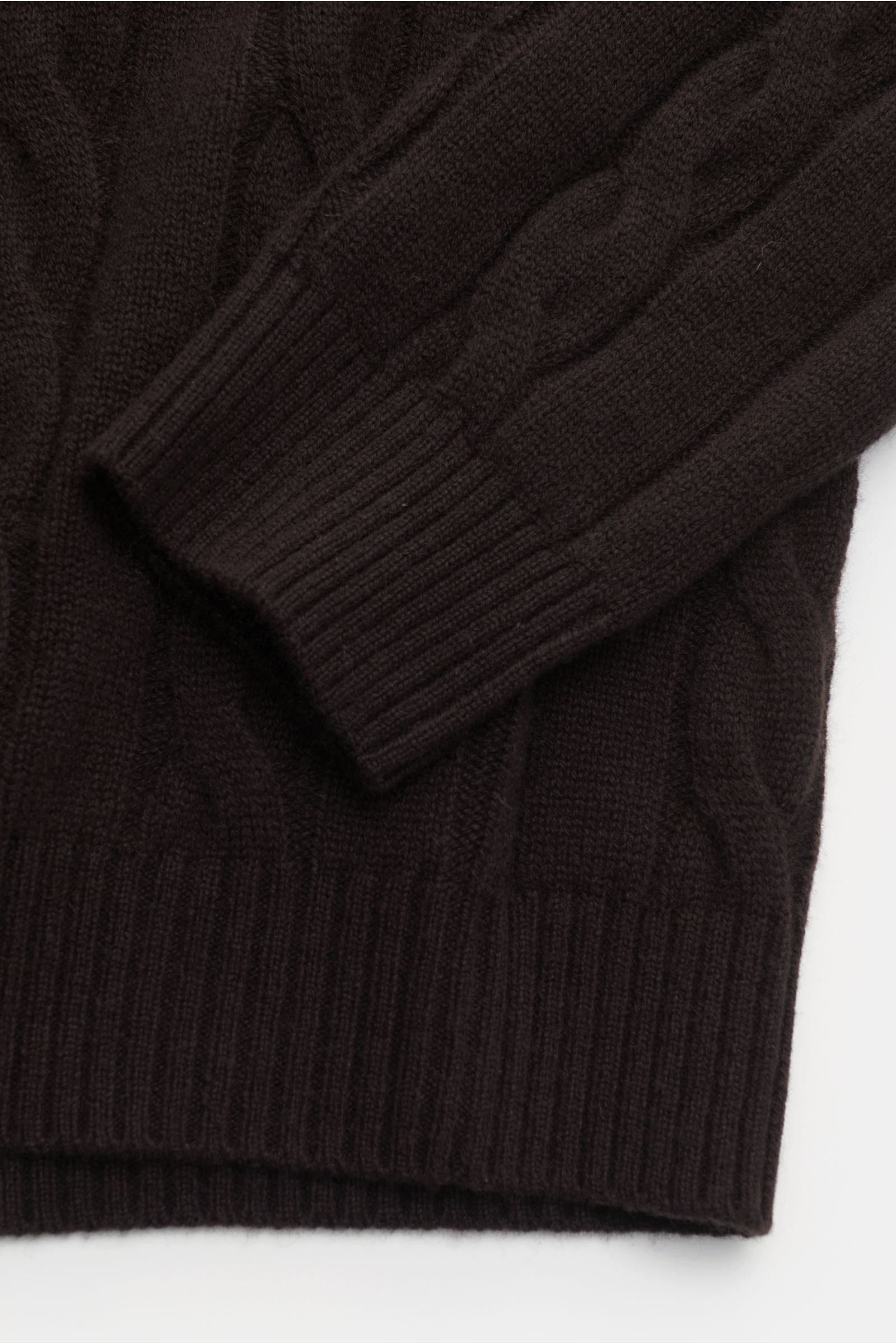 Nahaufnahme von Ärmel und Bund des von Braun Cashmere Rollkragenpullover dunkelbraun mit zeitlosem Zopfstrickmuster, weicher Griff, Regular Fit, anliegendem Rollkragen und flexiblen Rippbündchen, fotografiert von oben.