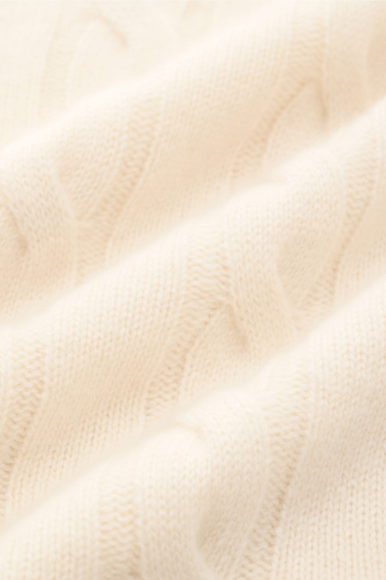 von Braun Cashmere Rollkragenpullover creme in Nahaufnahme, weiches, zeitloses Zopfstrickmuster aus reinem Cashmere mit anliegendem Rollkragen und flexiblen Rippbündchen, fotografiert aus schräger Perspektive.