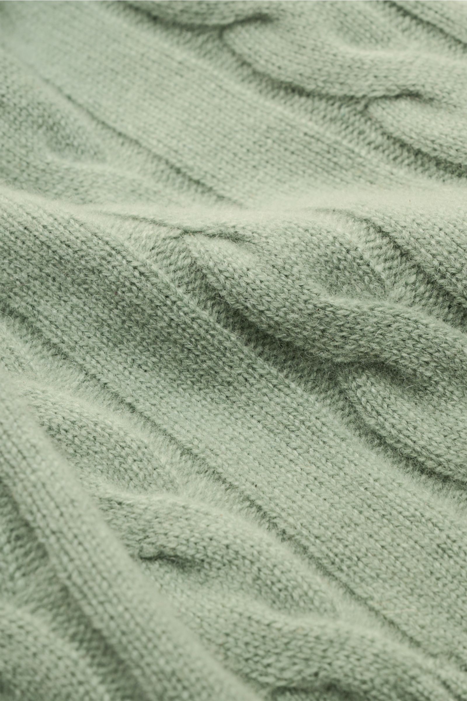 Nahaufnahme eines graugrünen von Braun Cashmere Rollkragenpullovers mit zeitlosem Zopfstrickmuster, weichem Griff, Regular Fit, anliegendem Rollkragen und flexiblen Rippbündchen, fotografiert aus leichter Schräge.