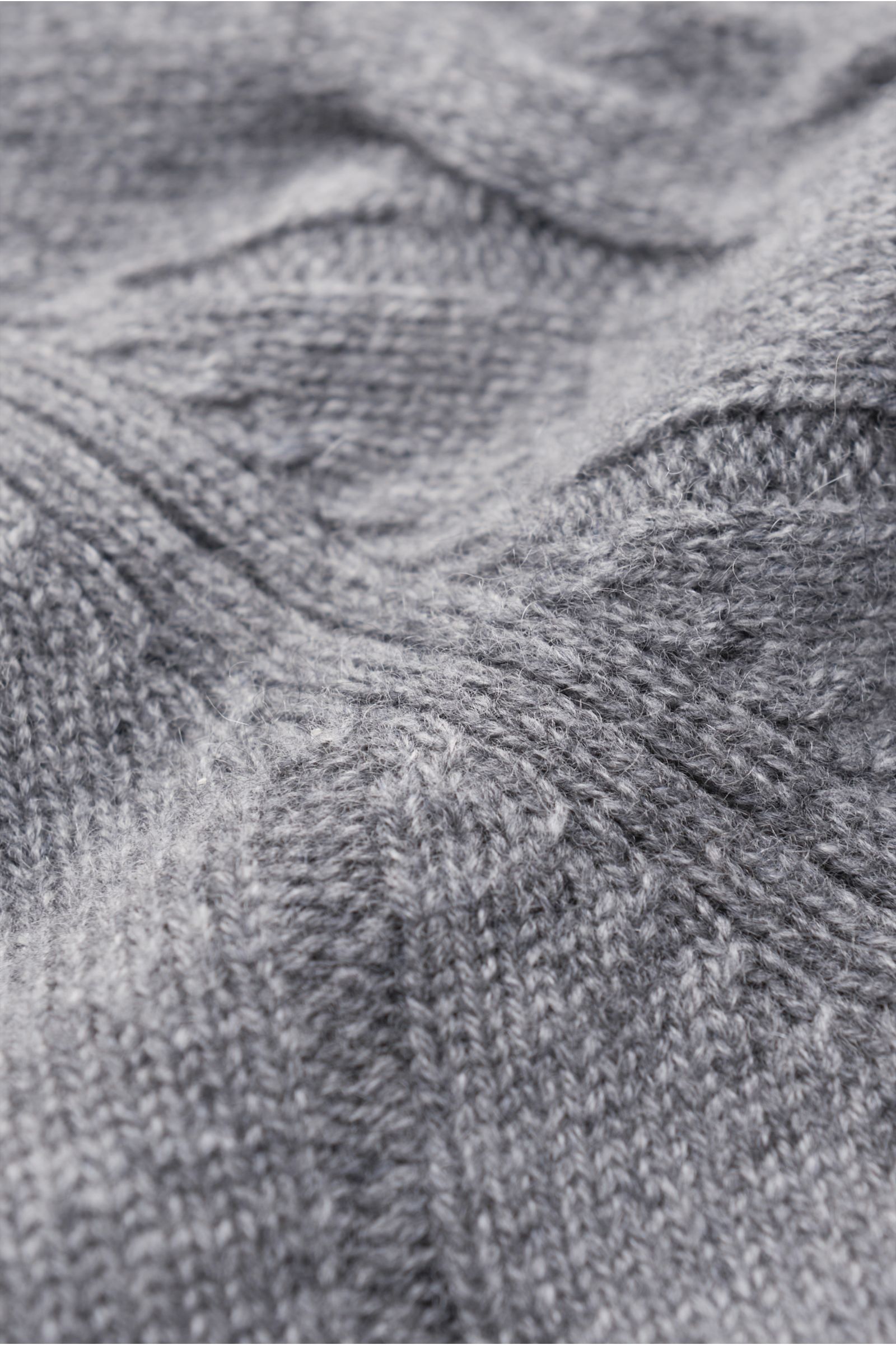 Nahaufnahme des von Braun Cashmere Rollkragenpullovers grau meliert, fotografiert aus schräger Perspektive, zeigt das klassische Zopfstrickmuster, weichen Griff und flexible Rippbündchen. Komfortabel durch die Winterzeit: Softer, zu einem klassischen Zopf