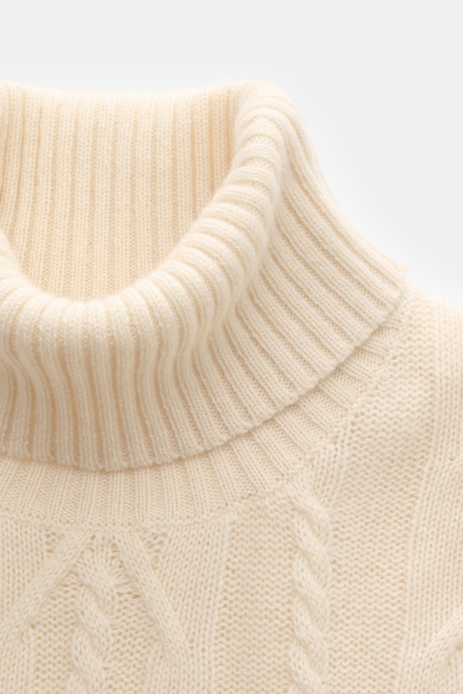 Nahaufnahme des von Braun Cashmere Rollkragenpullovers offwhite von oben, zeigt weichen, mittelfeinen Zopfstrick, Slim Fit und anliegenden Rollkragen.
