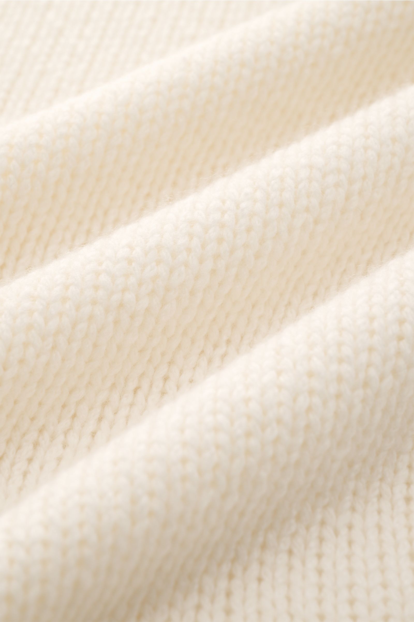 Detailaufnahme des groben Strickbilds und weichen Griffs des cremefarbenen 04651/ A trip in a bag Cashmere Rollkragenpullovers.