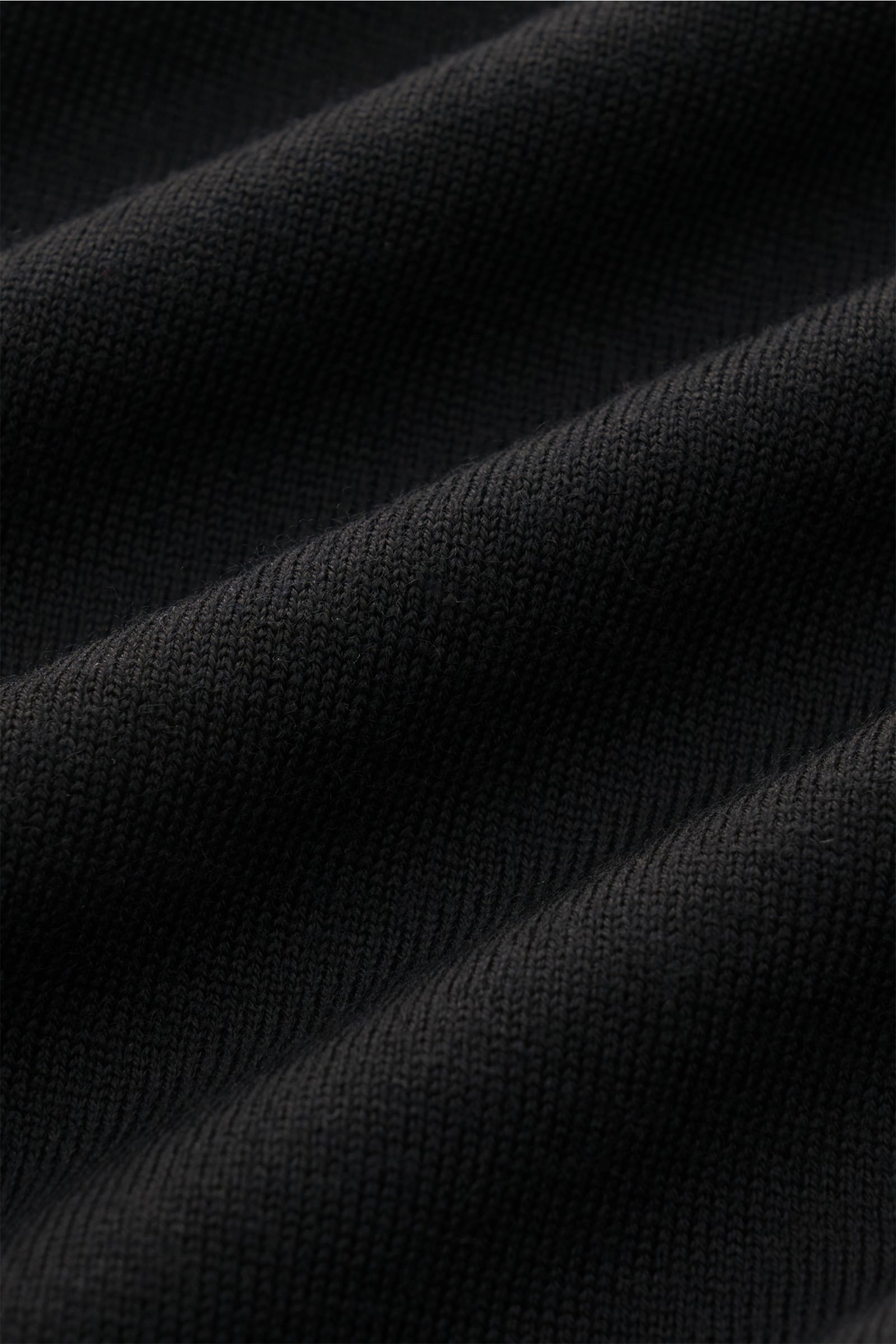 Nahaufnahme in schräger Perspektive des schwarzen 04651/ A trip in a bag Merino Feinstrick-Rundhalspullover mit feinem Strickbild und weichem Griff.