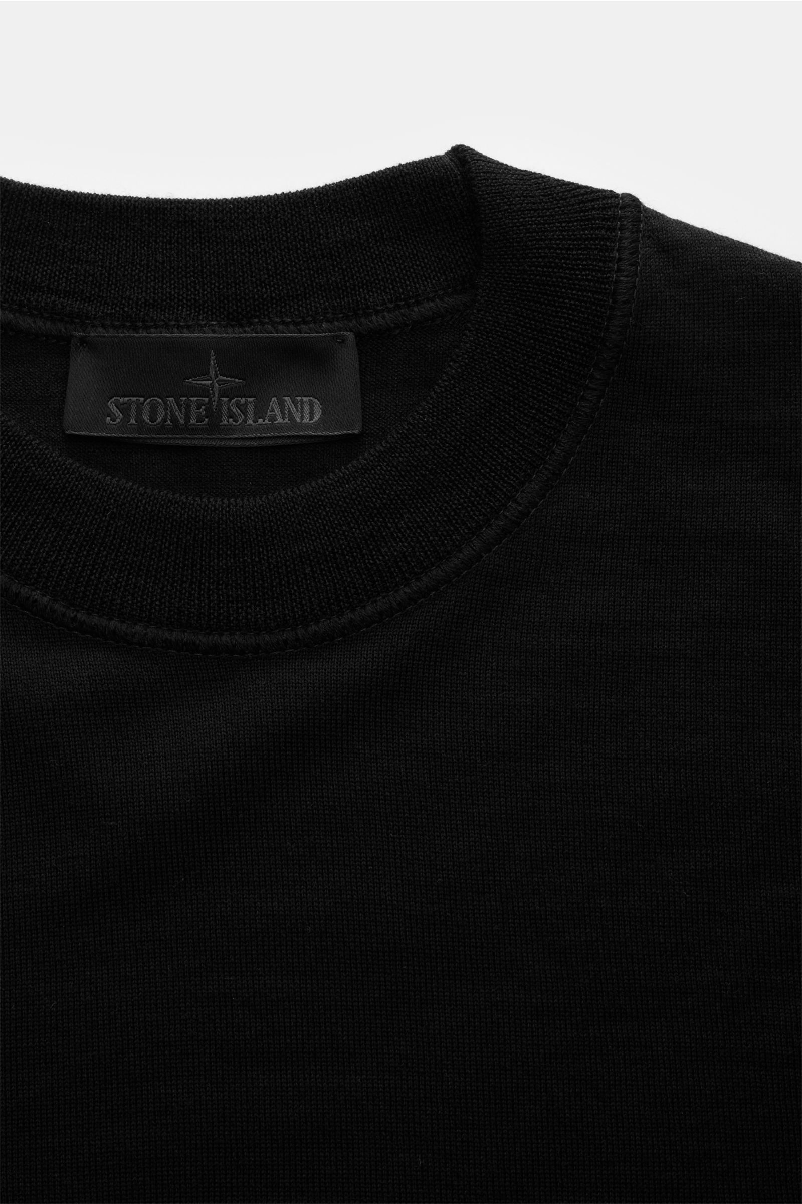 Stone Island Rundhalspullover 'Ghost Piece' schwarz, Slim Fit, aus reiner Wolle mit Rundhalsausschnitt, weichem Griff, feinem Strickbild, elastischen Bündchen, tonalem Kompass-Badge, Nahaufnahme von oben.
