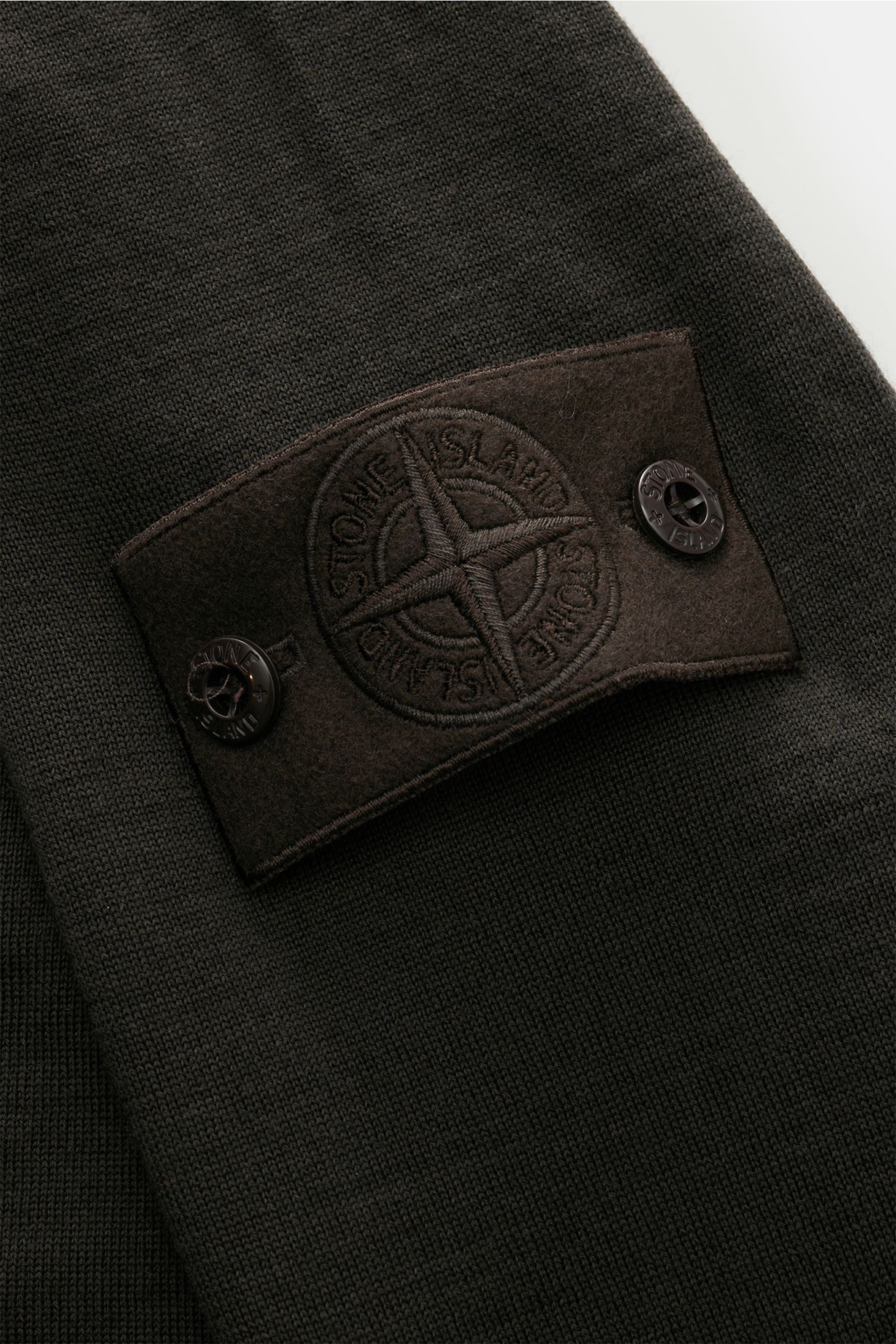 Stone Island Rundhalspullover 'Ghost Piece' dunkelbraun, Detailaufnahme des tonalen Kompass-Badges am Oberarm aus feinem Strick aus reiner Wolle.