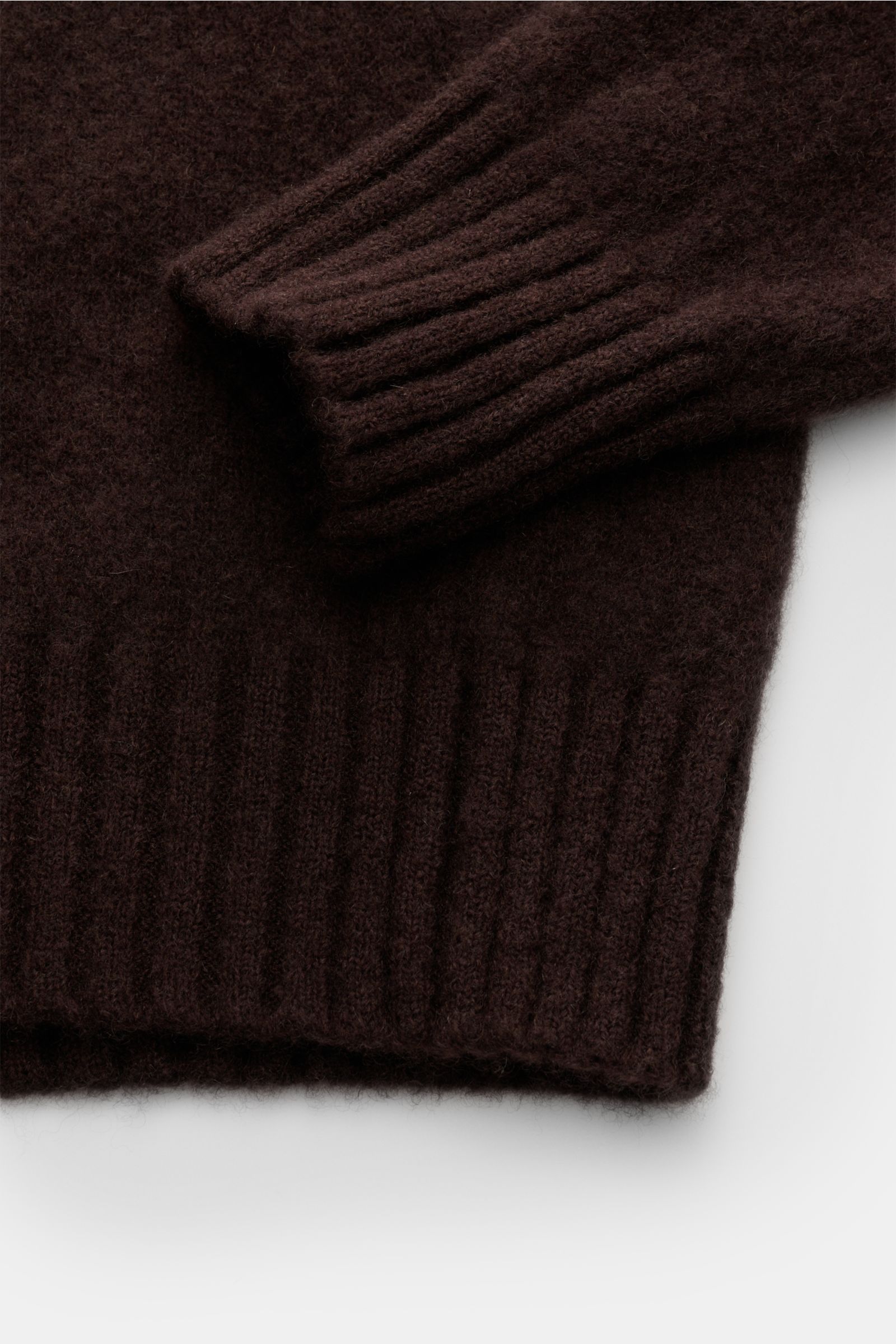 Close-up image of the sleeve and hem of the Piacenza 1733 Rundhalspullover dunkelbraun, showing its soft, dark brown knit fabric from a top-down perspective. Der wohl softeste Rundhalspullover der Saison kommt aus der italienischen Spinnerei PIACENZA –