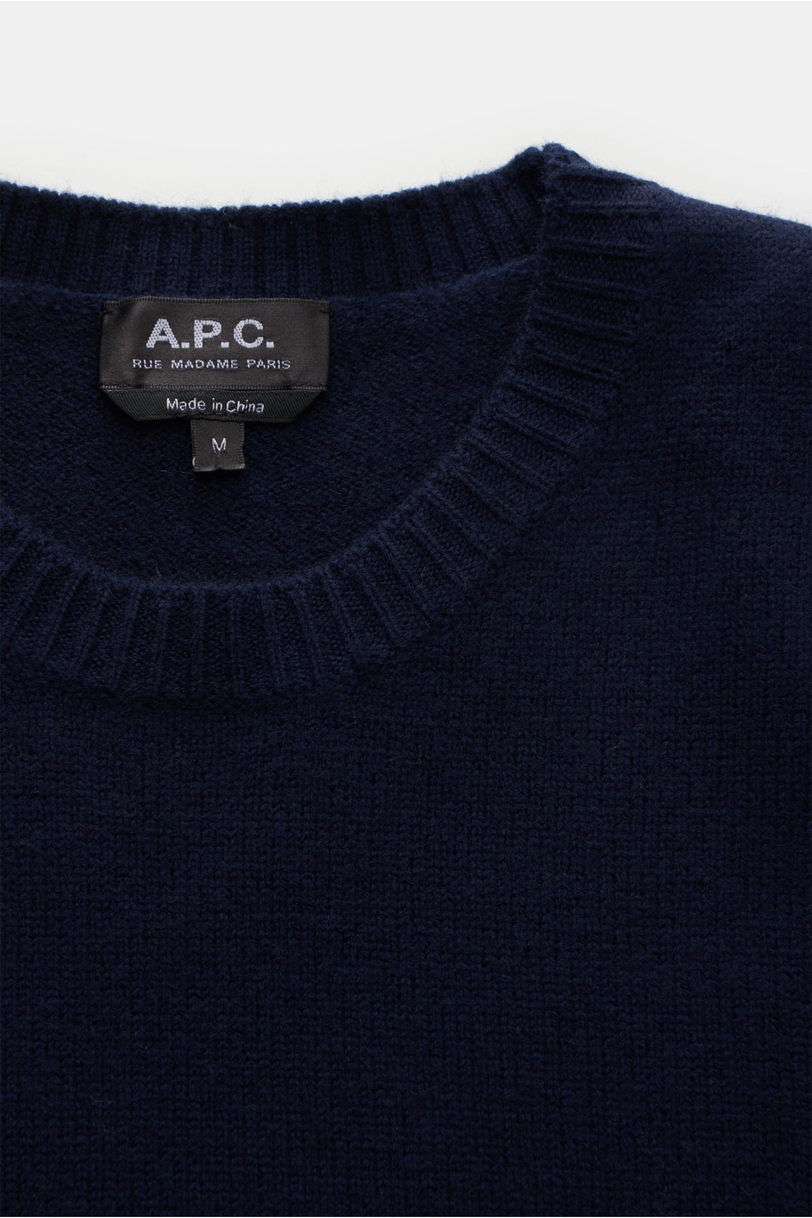 Close-up front view of A.P.C. Rundhalspullover 'Edward' navy, showing slim fit, reine Wolle, weicher Griff, mittelfeines Strickbild, flexible Rippbündchen, and dezentes Logo auf der Vorderseite.