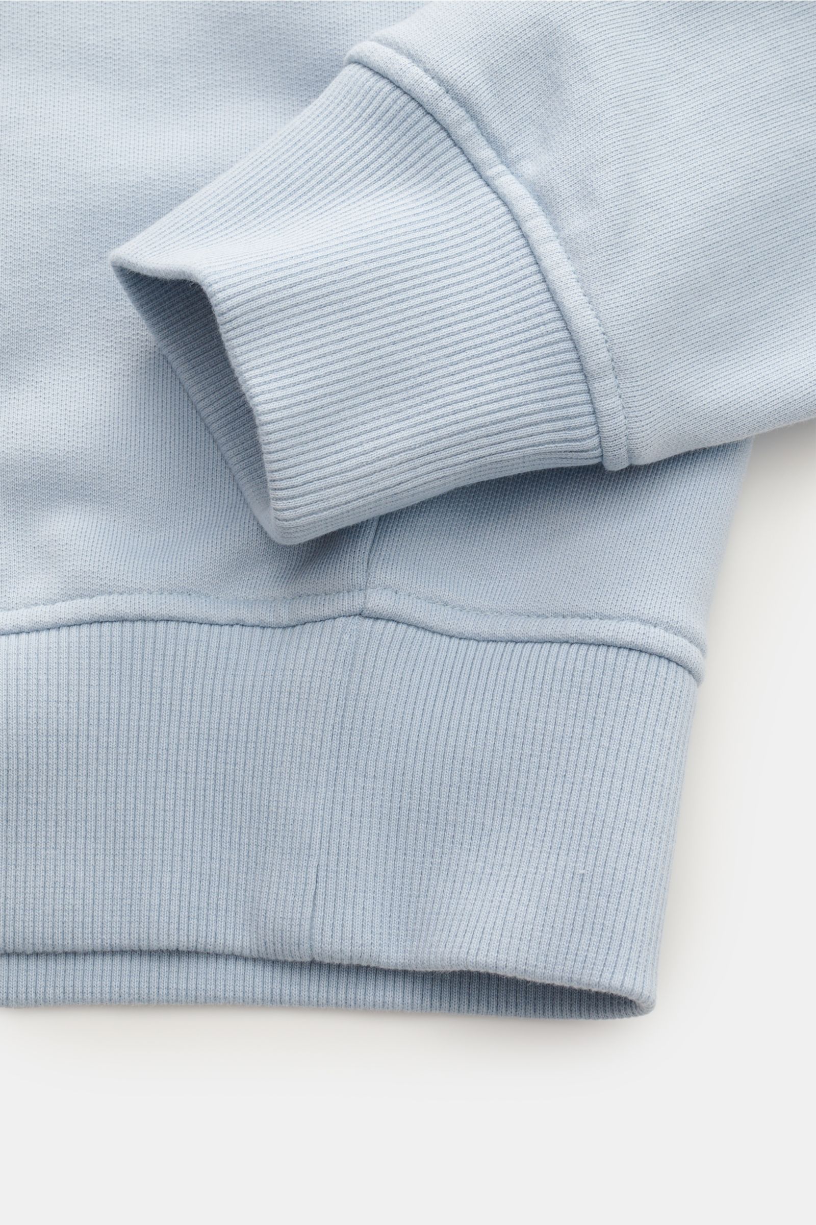 Close-up image of the Ami Paris Rundhals-Sweatshirt hellblau showing the ribbed cuff and hem from a side angle, highlighting the high-quality cotton fabric and stitching details. Ein dezentes Herz-Stitching auf der Brust wertet dieses Basic-Sweatshirt 