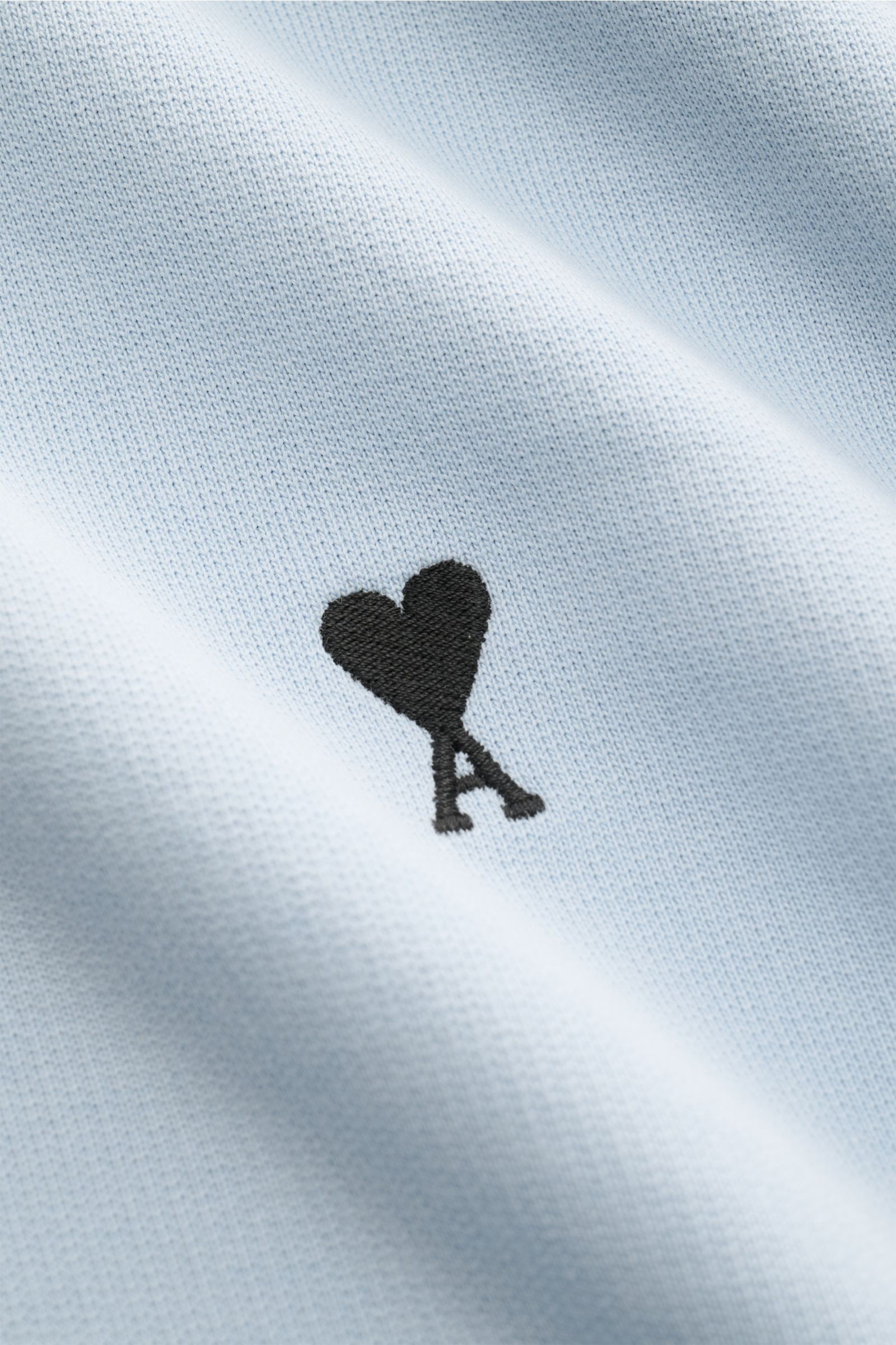 Close-up front view of Ami Paris Rundhals-Sweatshirt hellblau showing light blue cotton fabric with subtle heart-stitching on the chest, featuring pure cotton sweat, light stretch, textured feel, unisex oversized fit, round neckline, rear AMI stitching, a