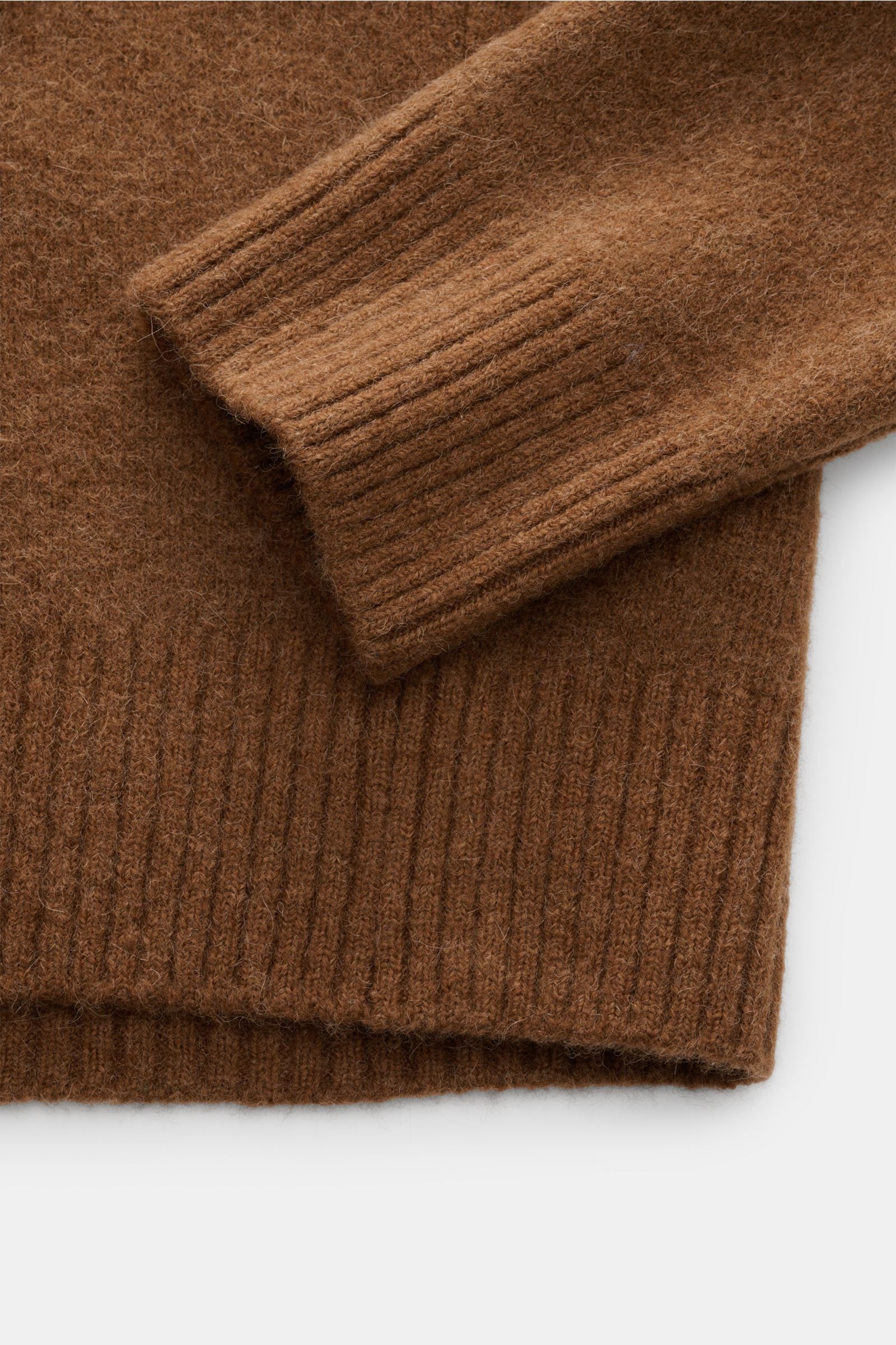 Nahaufnahme des hellbraunen Ami Paris Rundhalspullover mit elastischem Strick aus Alpaka, Wolle, Microfaser, weichem Griff, breiten Rippbündchen, Oversized Fit, Rundhalsausschnitt, eingestricktem Herz-Logo, fotografiert von oben auf Ärmel und Bund.