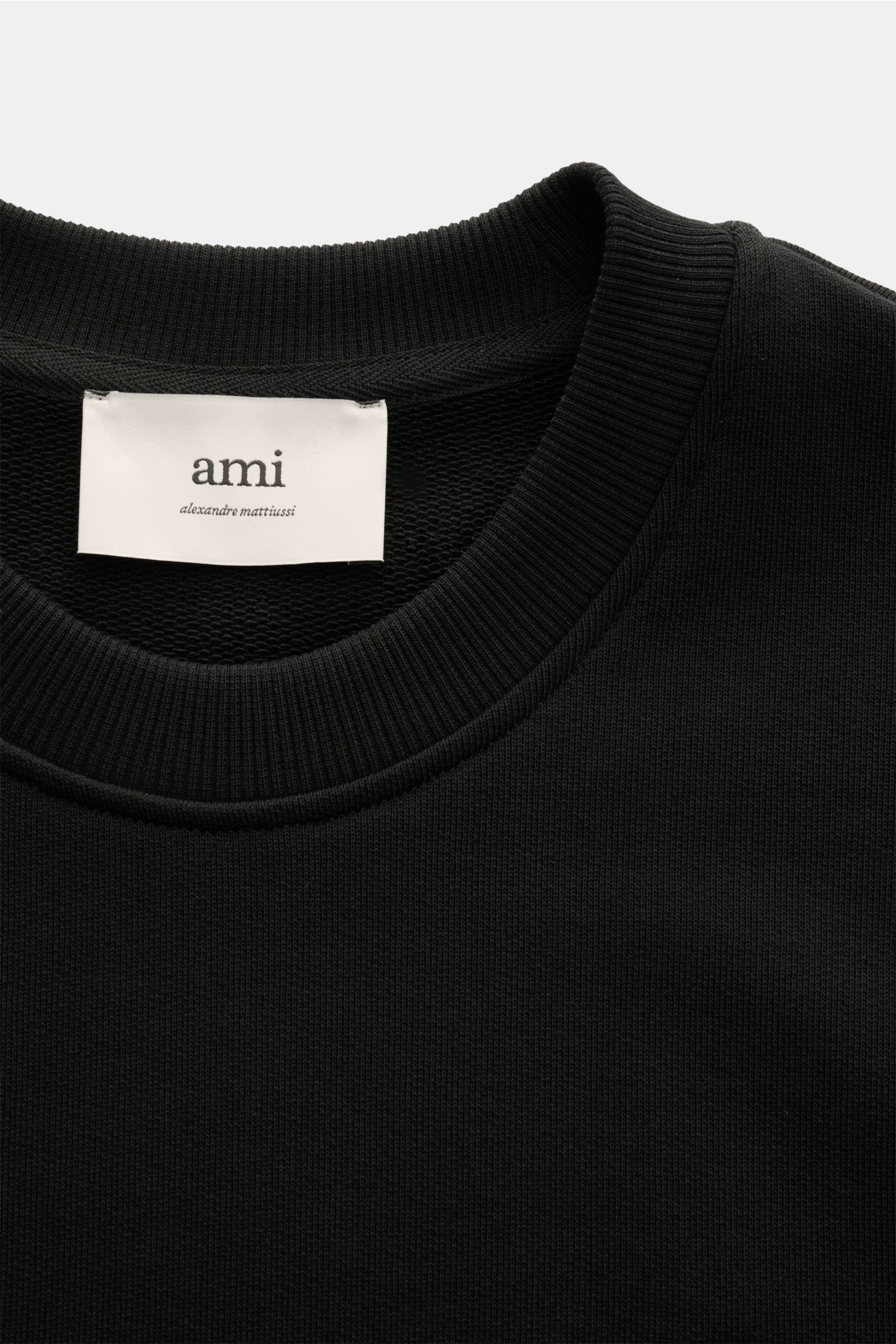 Close-up front view of the Ami Paris Rundhals-Sweatshirt schwarz showing its ribbed round neckline and white label, made of slightly stretchy organic cotton with heart stitching on the chest, unisex oversized fit, comfortable ribbed cuffs, and rear AMI st