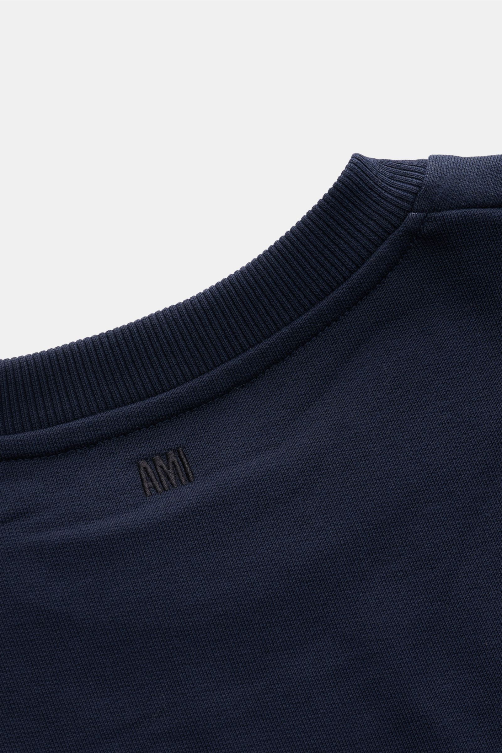 Close-up image of the back neckline of the Ami Paris Rundhals-Sweatshirt dunkelblau, showing ribbed collar and subtle black AMI stitching on dark blue organic cotton fabric. Love is in the air! Das markentypische Herz-Stitching auf der Brust wertet dieses