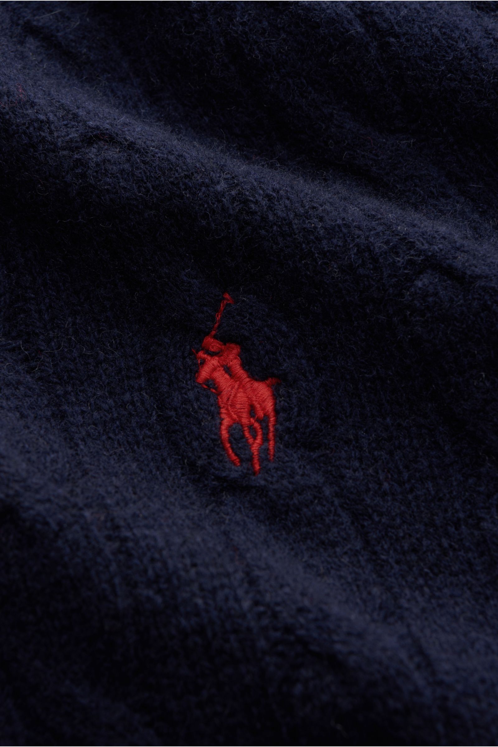 Close-up front view of the Polo Ralph Lauren Rundhalspullover dunkelblau showing its red Polospieler-Stitching on dark blue wool and cashmere blend with textured cable knit pattern. This classic features a soft feel, fine knit, slim fit, round neckline, a