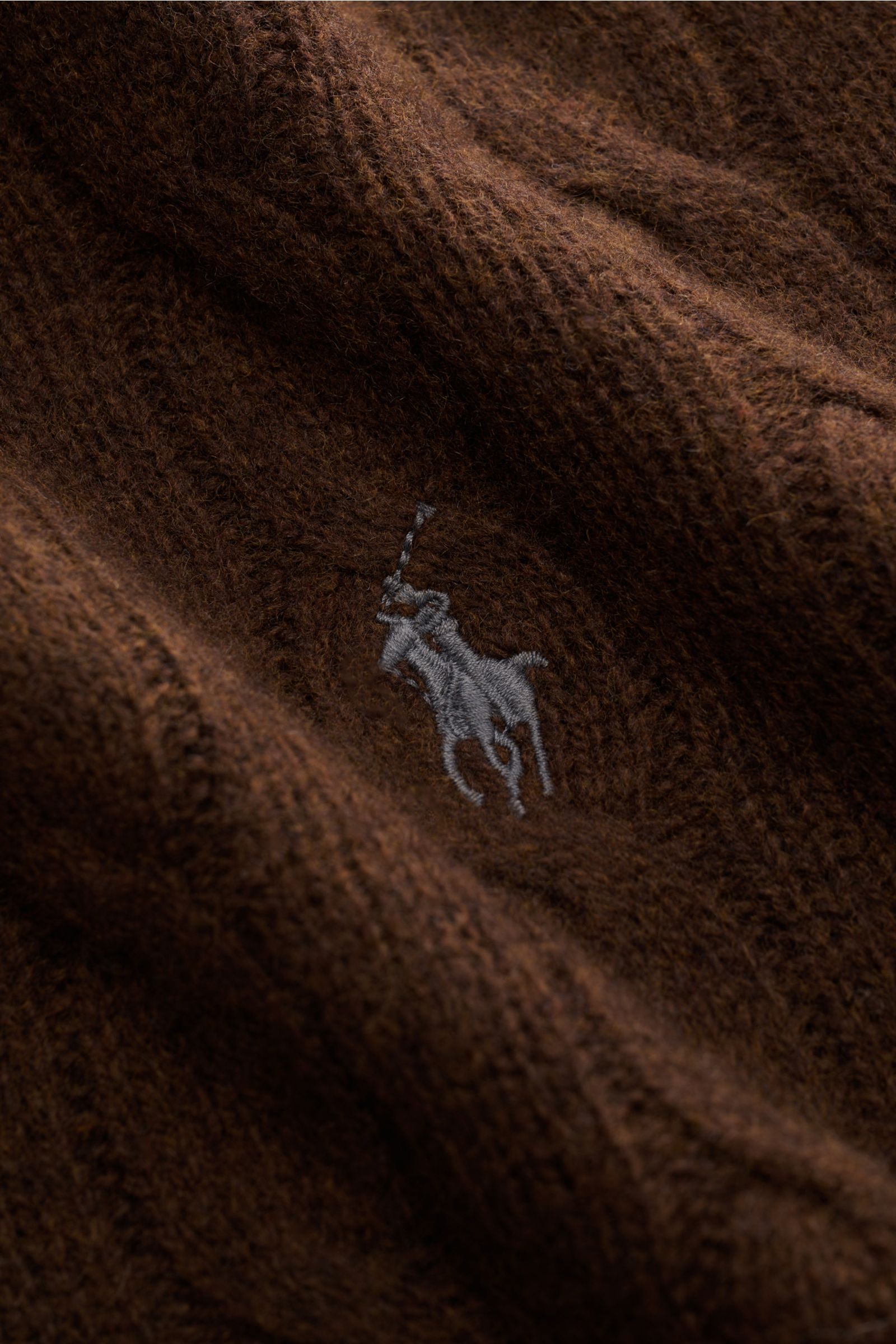 Nahaufnahme des braunen Polo Ralph Lauren Rundhalspullovers aus Wolle und Cashmere mit Zopfmuster und Polospieler-Stitching.