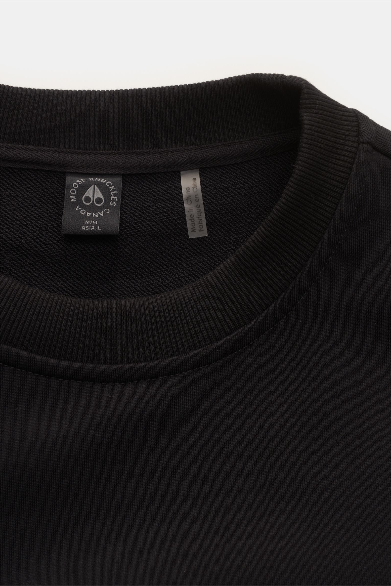 Moose Knuckles Sweatshirt 'Hartsfield Crew' schwarz, Detailaufnahme von oben, Rundhalsausschnitt, reiner Baumwolle, Metall-Logo-Patch am Oberarm, weicher Griff, Regular Fit, flexible Rippbündchen, MOOSE KNUCKLES-Weblabel am Saum.