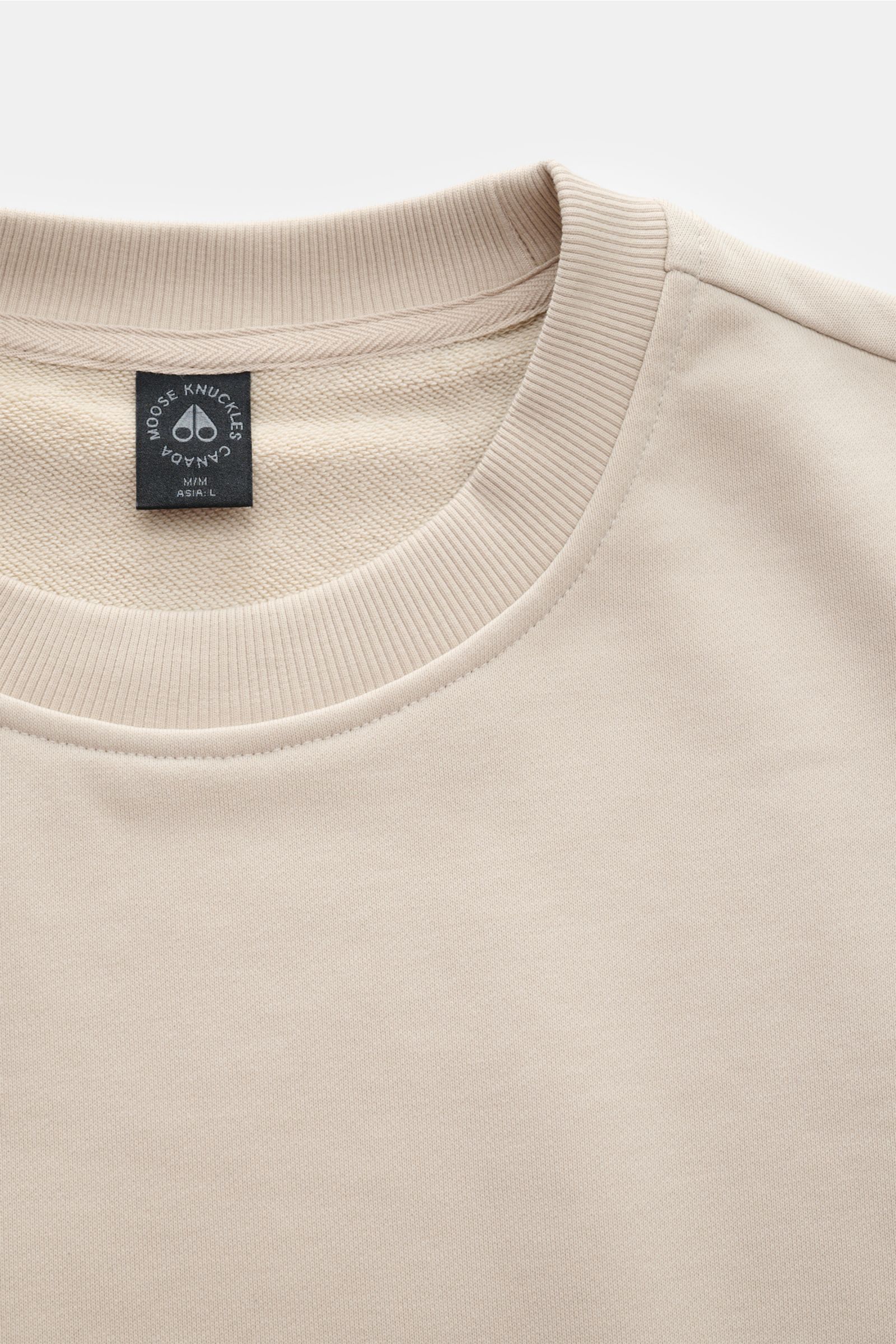 Moose Knuckles Sweatshirt 'Hartsfield Crew' creme, Nahaufnahme von oben, Rundhalsausschnitt, weicher Baumwollstoff, metallisches Logo-Patch am Oberarm, flexible Rippbündchen, Regular Fit, Weblabel am Saum.