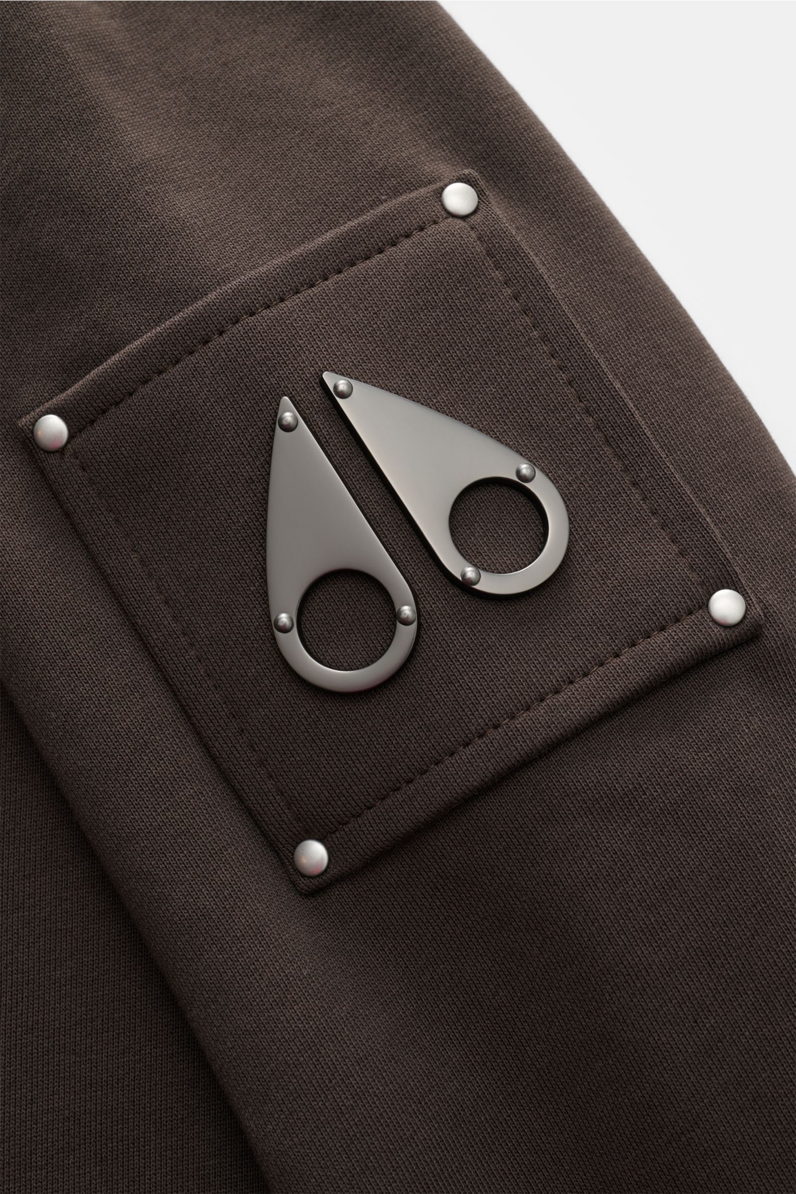 Close-up of the upper arm patch on Moose Knuckles Sweatshirt 'Hartsfield Crew' graubraun showing the metal logo on soft gray-brown cotton fabric from a side angle.

Veredelte Sportswear: Auf dem Oberarm des Sweatshirts 'Hartsfield Crew' aus reiner Baum