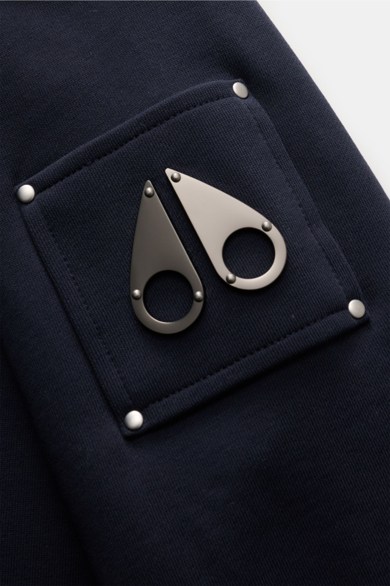 Nahaufnahme des Patches mit metallischem MOOSE KNUCKLES-Logo auf dem Oberarm des navyfarbenen Moose Knuckles Sweatshirts 'Hartsfield Crew' aus reiner Baumwolle.