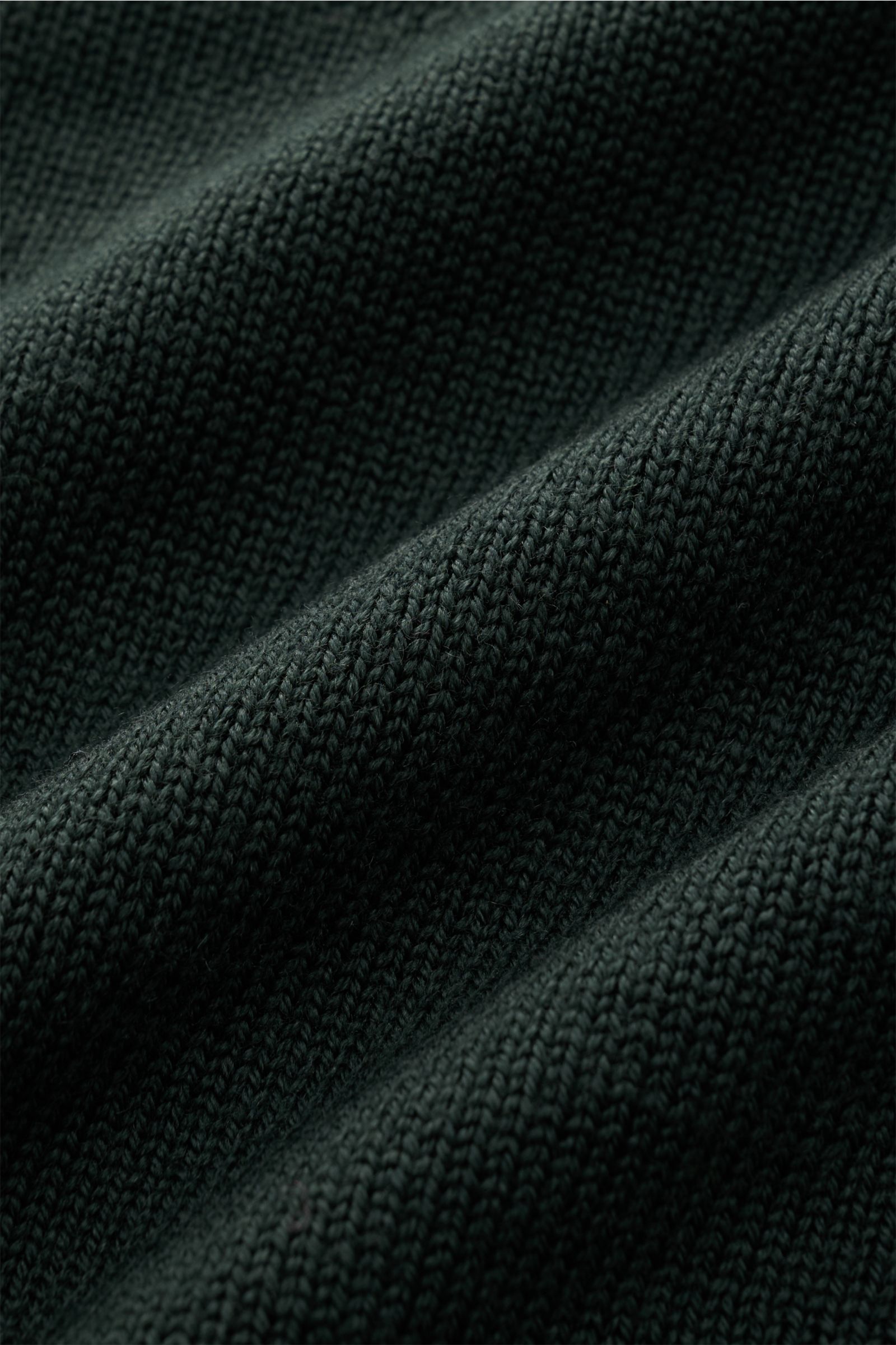 Nahaufnahme des dunkelgrünen B.F. Knitwear Merino Rundhalspullovers mit weichem Griff, mittelgrobem Strickbild, Slim Fit, Rundhalsausschnitt und flexiblen Rippstrick-Bündchen aus reiner Merinowolle.