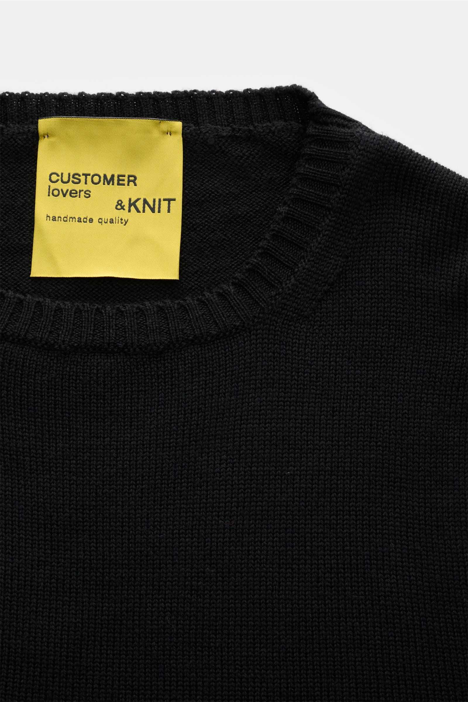 Nahaufnahme des B.F. Knitwear Merino Rundhalspullover schwarz, von oben fotografiert, reine Merinowolle, weicher Griff, mittelgrobes Strickbild, Slim Fit, Rundhalsausschnitt, flexible Rippstrick-Bündchen.