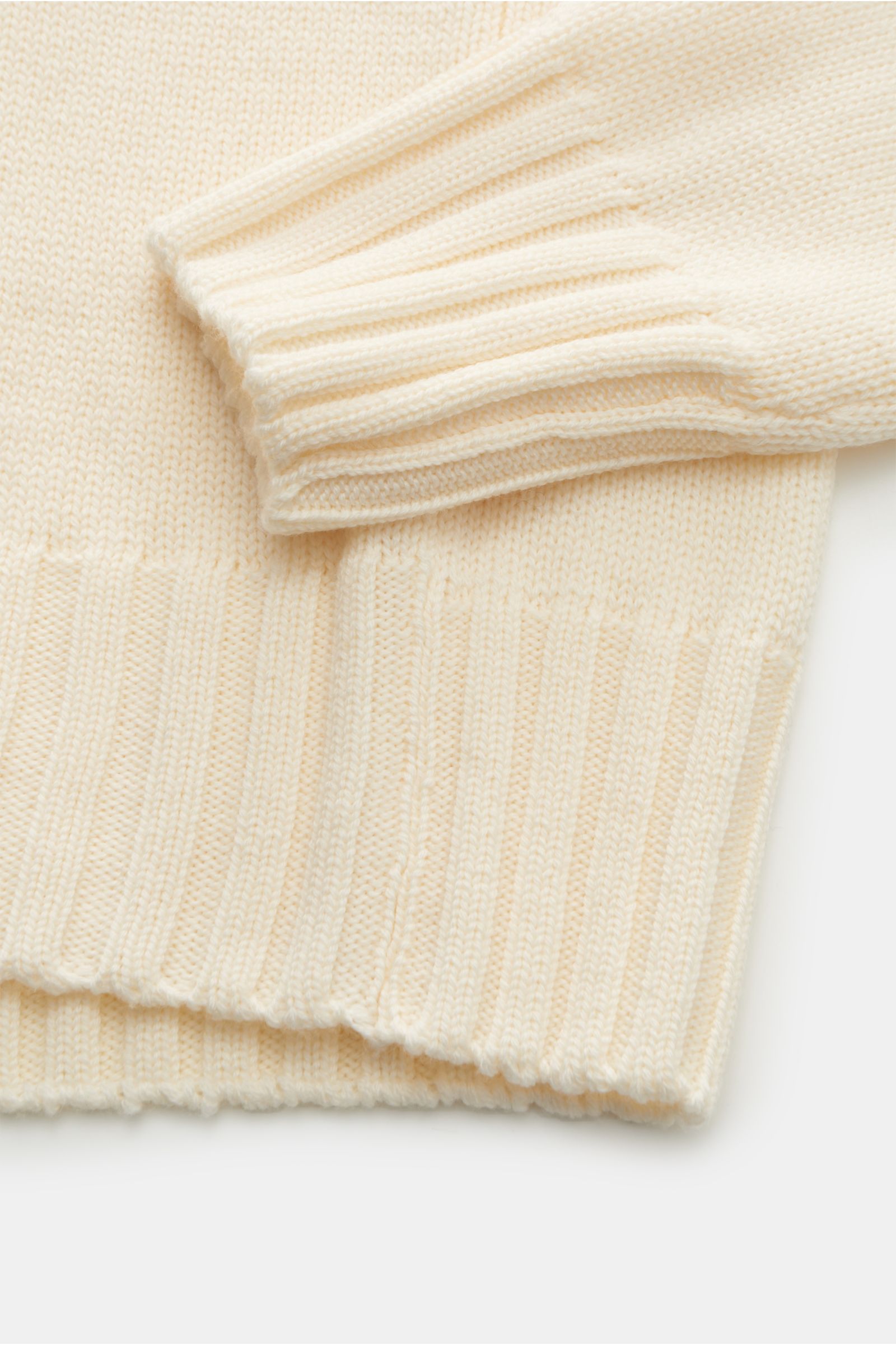 Close-up image of the B.F. Knitwear Merino Rundhalspullover creme, showing the sleeve and hem from a top-down perspective, featuring reine Merinowolle, weicher Griff, mittelgrobes Strickbild, Slim Fit, Rundhalsausschnitt, and breite Rippstrick-Bündchen.