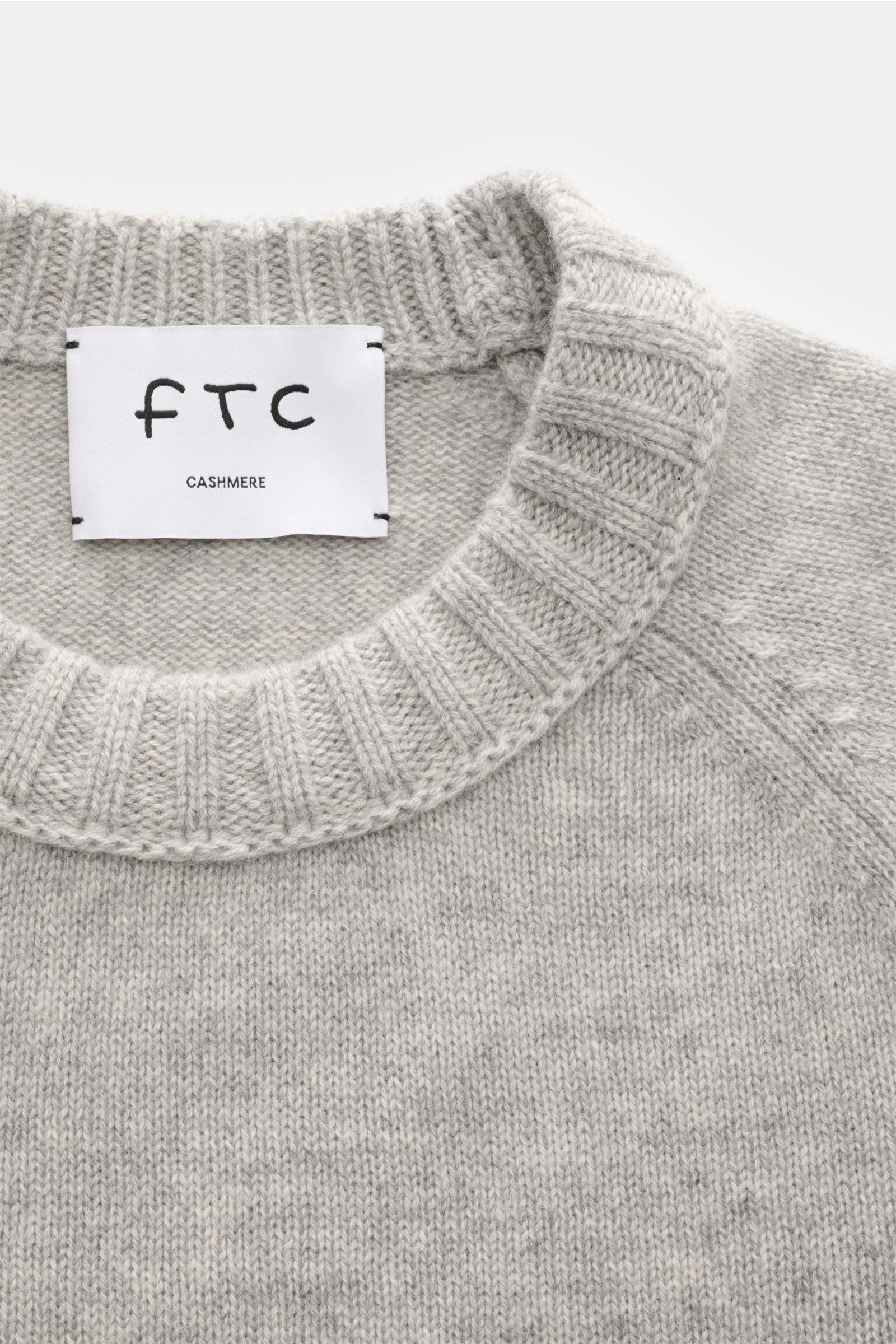 Close-up front view of FTC Cashmere crew neck jumper grey mottled, showing ribbed crew neck, raglan sleeves, medium-fine knit, and label. Pure fair trade cashmere, OEKO-TEX® certified, very soft feel, slim fit, comfortable ribbed bands.