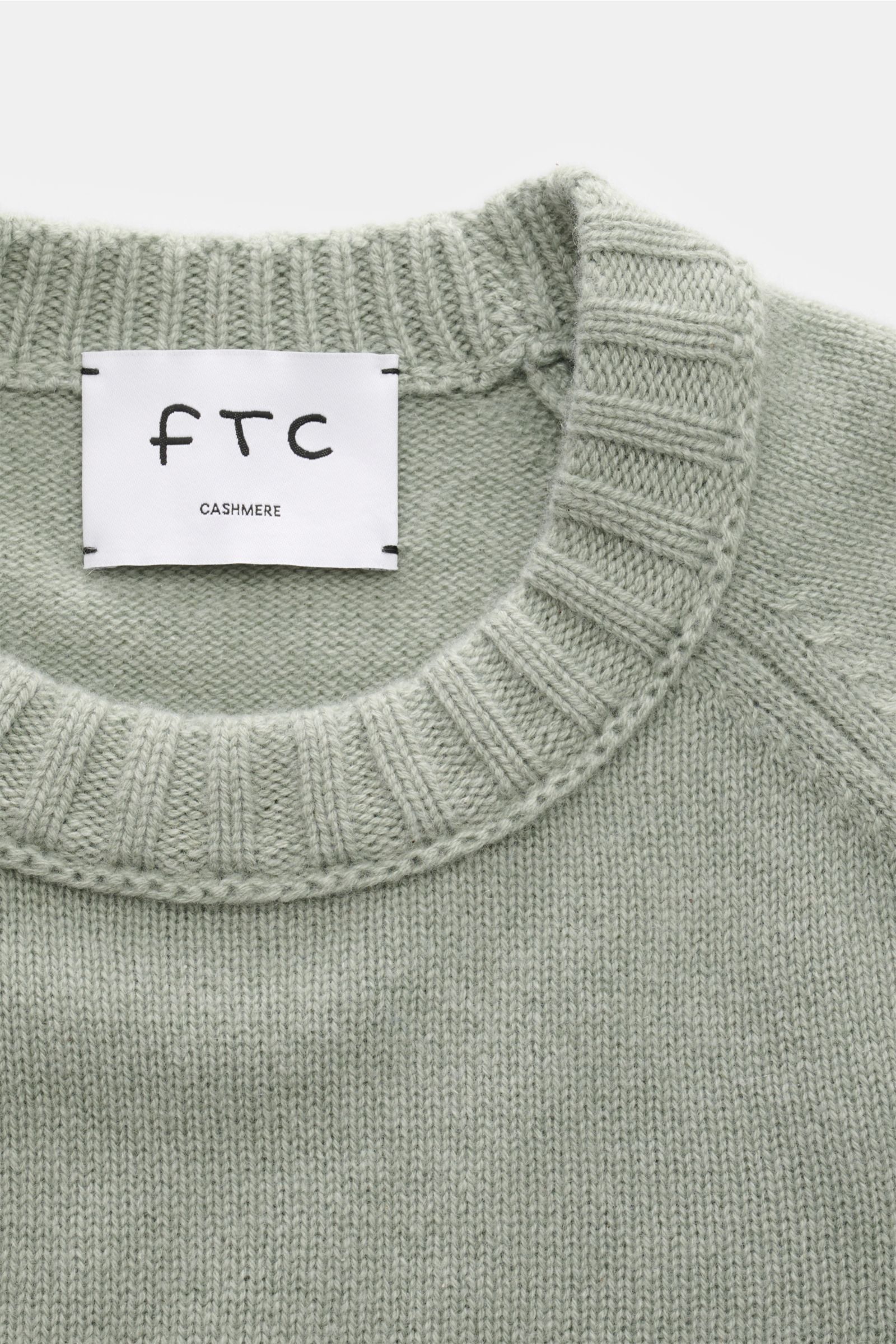 Nahaufnahme des FTC Cashmere Rundhalspullover graugrün von oben, reiner Fair-Trade-Cashmere, OEKO-TEX® zertifiziert, sehr weicher Griff, mittelfeines Strickbild, Slim Fit, Rundhalsausschnitt, Raglanärmel, komfortable Rippbündchen.