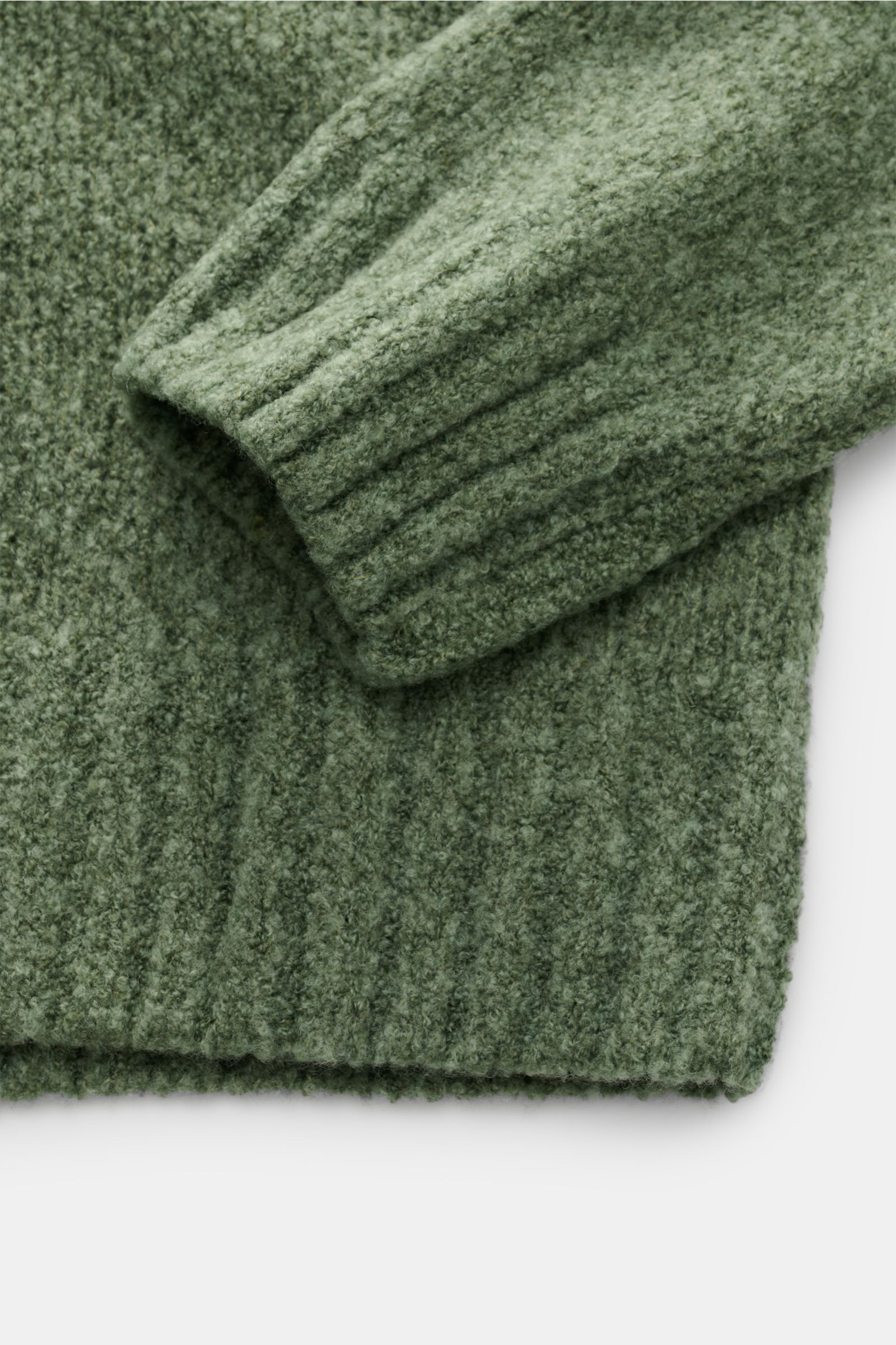 Nahaufnahme des Ärmelendes und Saums des graugrünen 04651/ A trip in a bag Rundhalspullover 'Grainy Crew' mit weicher Bouclé-Struktur.