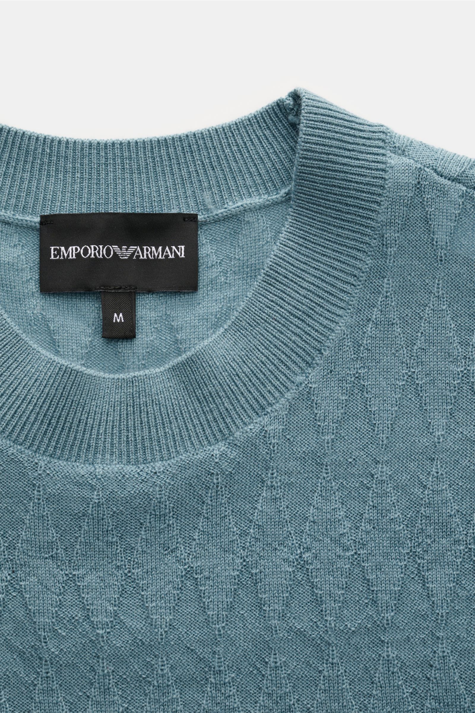 Nahaufnahme des Emporio Armani Rundhalspullover rauchblau von oben, zeigt feines Strukturstrick-Rautenmuster, Rundhalsausschnitt und Weblabel.