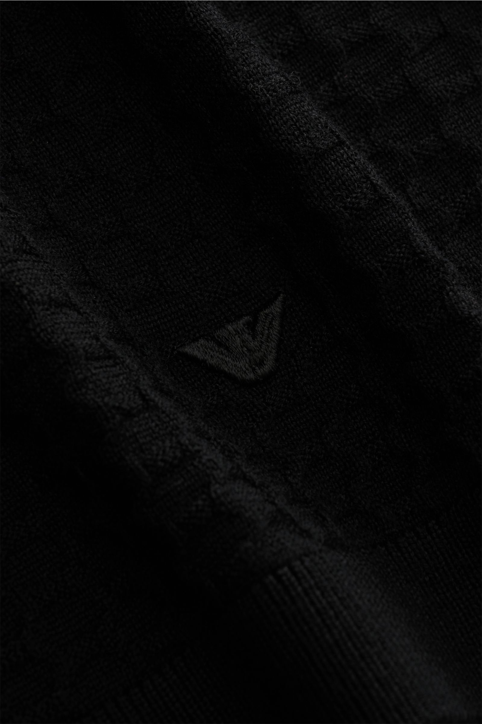 Emporio Armani Rundhalspullover schwarz, Nahaufnahme schräg von oben, reine Schurwolle, feines Strukturstrickmuster, Weblabel am Saum, Rippbündchen.