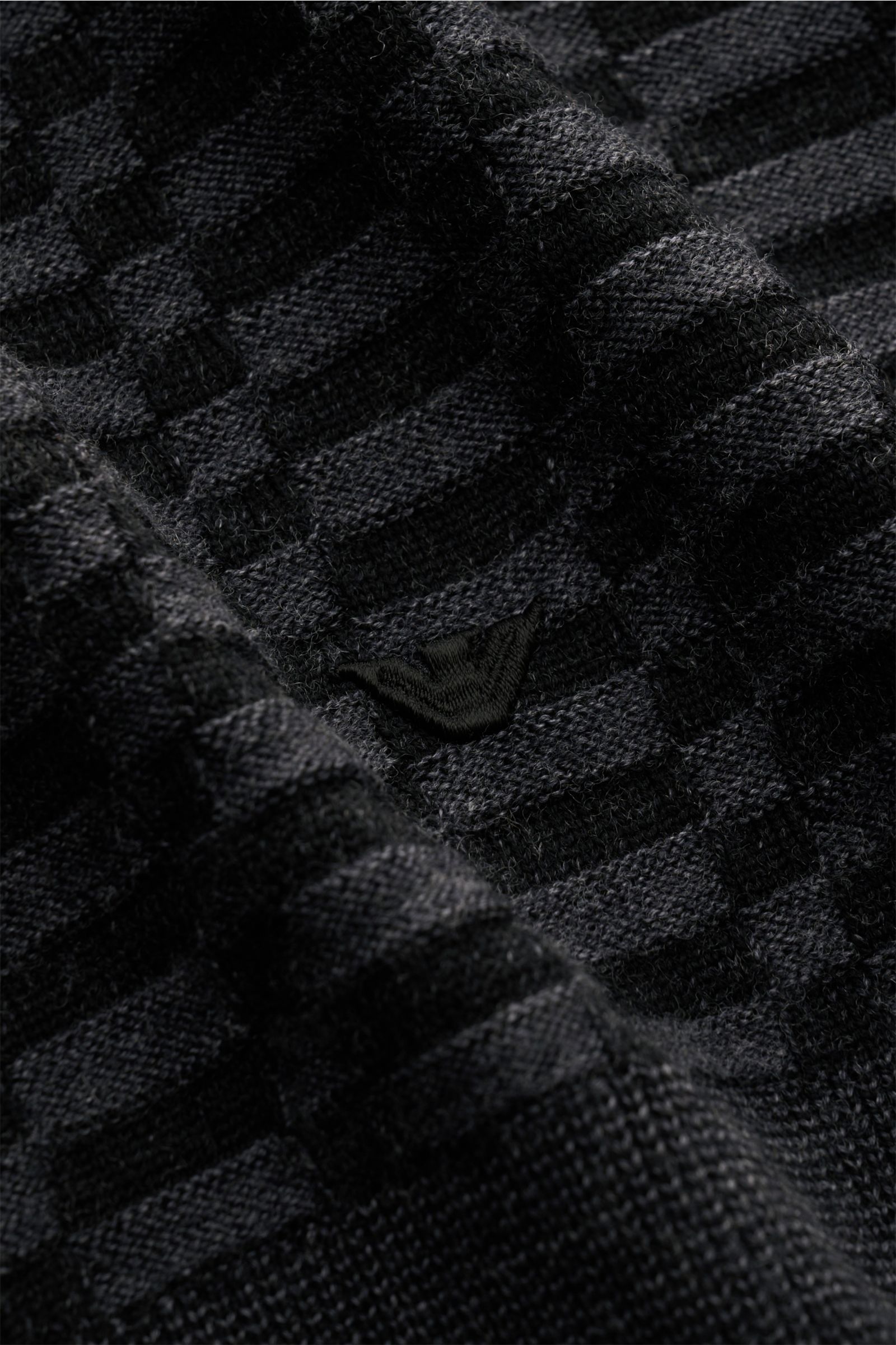 Nahaufnahme des Emporio Armani Rundhalspullover schwarz/dunkelgrau gemustert aus leichter Schurwolle mit feinem Strickbild, Rippbündchen und Weblabel am Saum.