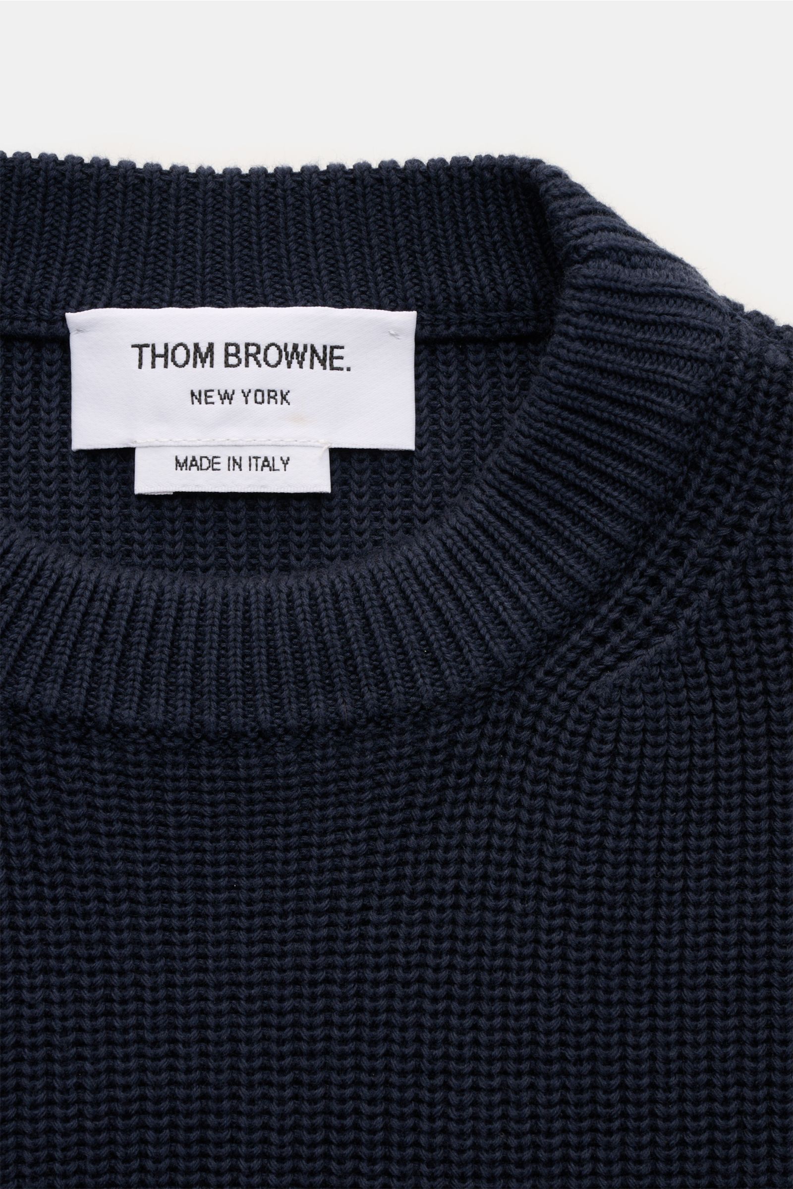 Close-up of the neckline and label of the Thom Browne Rundhalspullover graublau, showing a medium-knit, slim fit cotton crewneck sweater with soft texture, photographed from above. Stilvoll durch die kalte Saison: Der Rundhalspullover aus reiner Baumwolle