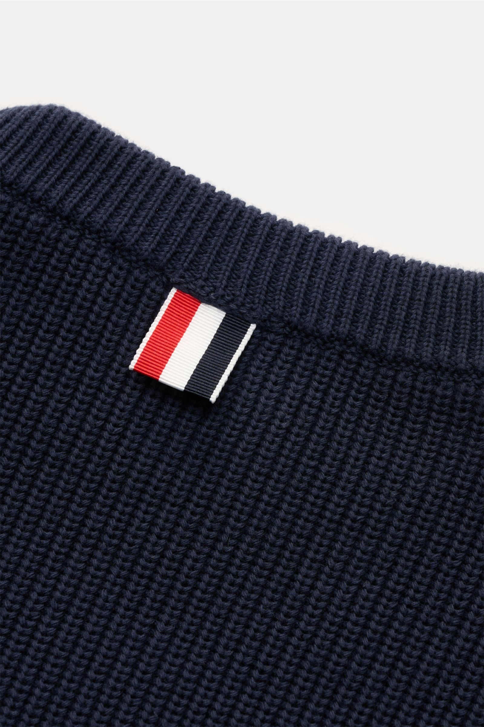 Thom Browne Rundhalspullover graublau shown from a close-up top angle, highlighting pure cotton knit, soft texture, ribbed round neckline, and signature tri-color label. Stilvoll durch die kalte Saison: Der Rundhalspullover aus reiner Baumwolle von THO