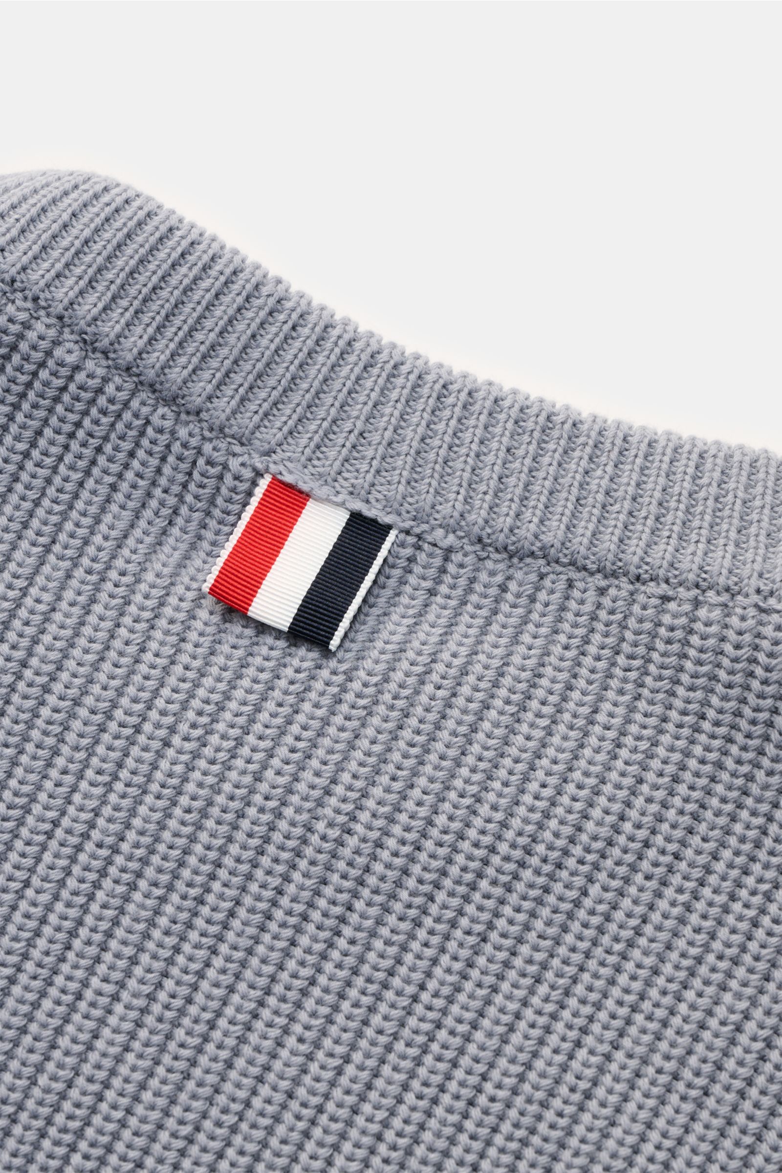 Close-up top-down view of the Thom Browne Rundhalspullover rauchblau showcasing ribbed neckline and signature tricolor tag on soft pure cotton knit.

Stilvoll durch die kalte Saison: Der Rundhalspullover aus reiner Baumwolle von THOM BROWNE setzt mit s