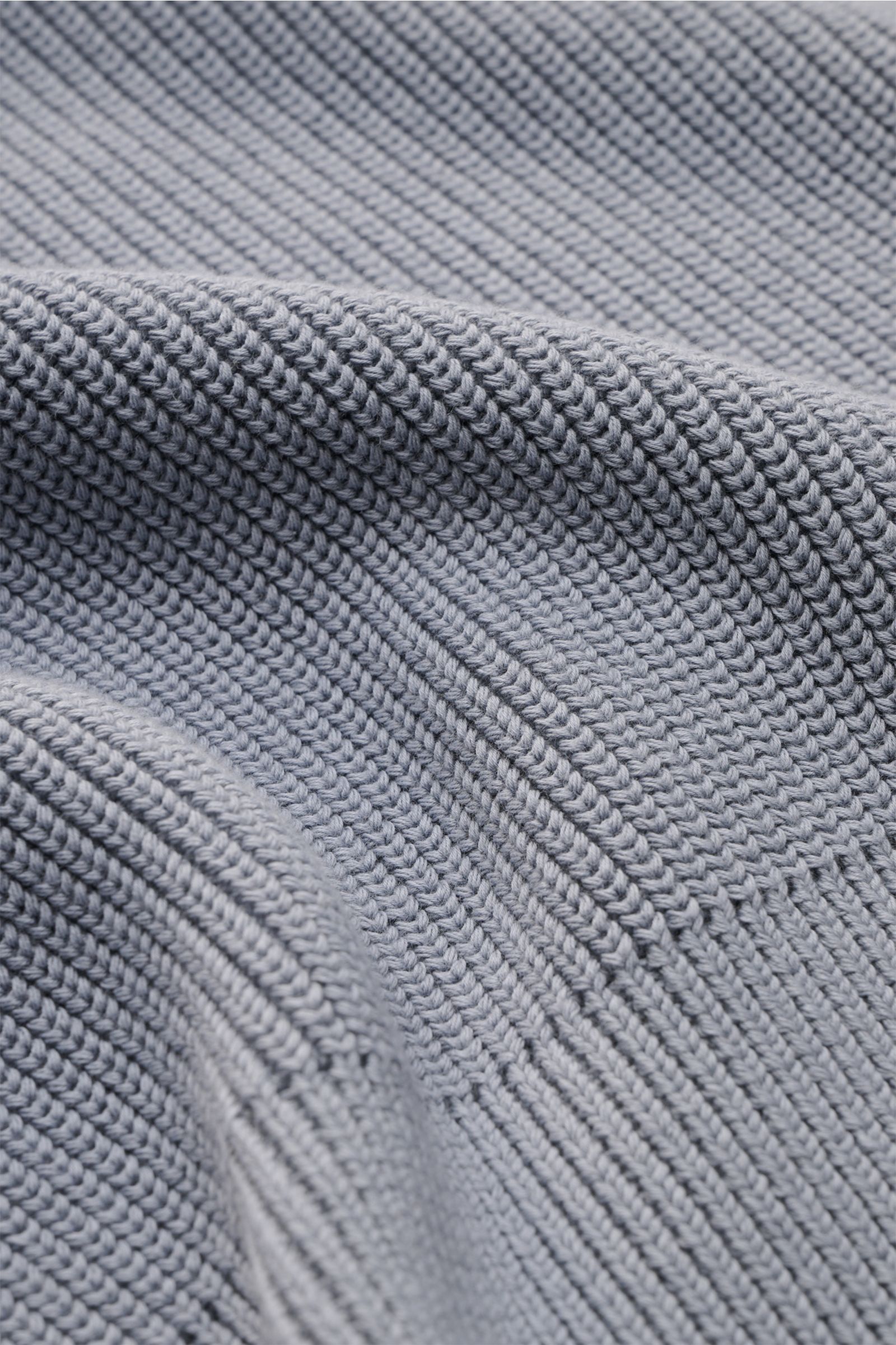 Close-up front view of Thom Browne Rundhalspullover rauchblau showing its pure cotton, soft texture, medium knit, slim fit, round neck, side slits, buttoned cuffs, and tonal sleeve stripes. Stilvoll durch die kalte Saison: Der Rundhalspullover aus rein