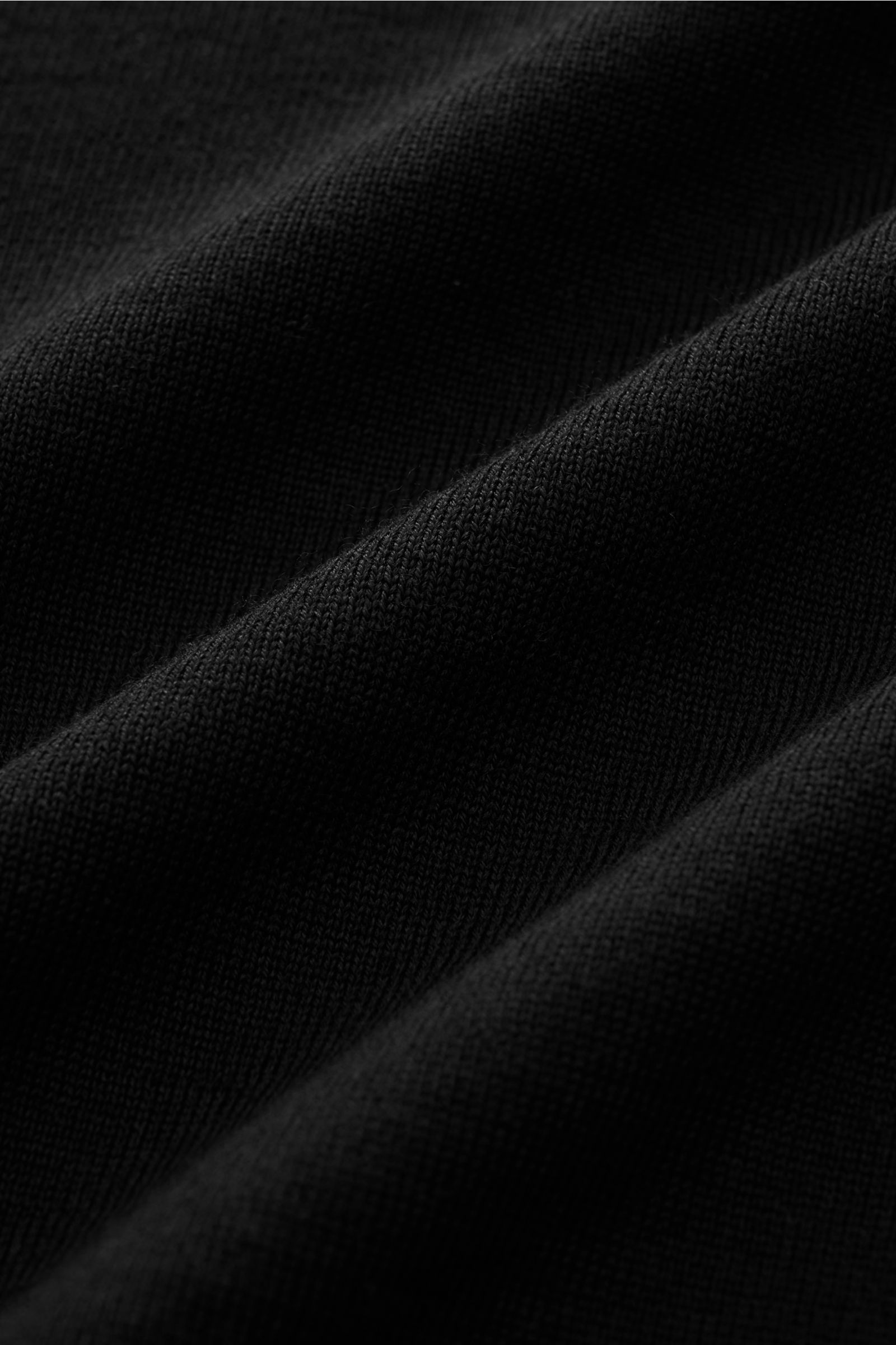 Stone Island Rundhalspullover 'Ghost Piece' schwarz, Slim Fit, feines Strickbild aus Wolle mit tonalem Kompass-Badge, Detailaufnahme Stoffstruktur.