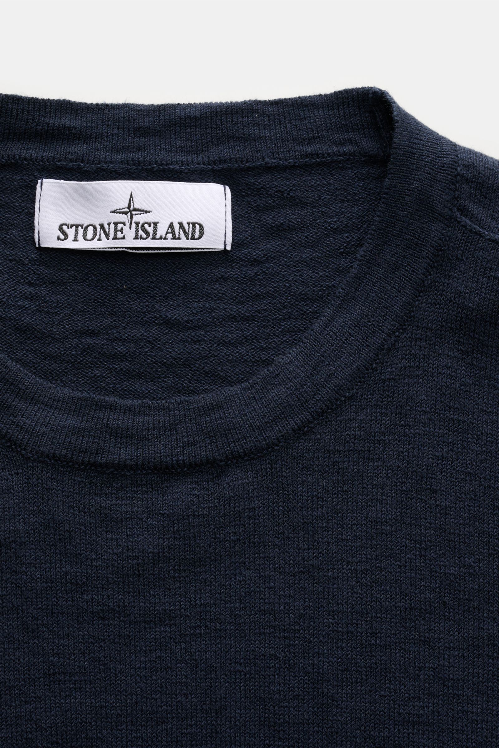 Stone Island Rundhalspullover navy in Slim Fit, aus Baumwoll-Microfaser-Mix mit feinem Strickbild, rolliertem Saum, Nähten und Kompass-Badge, Nahaufnahme von oben.