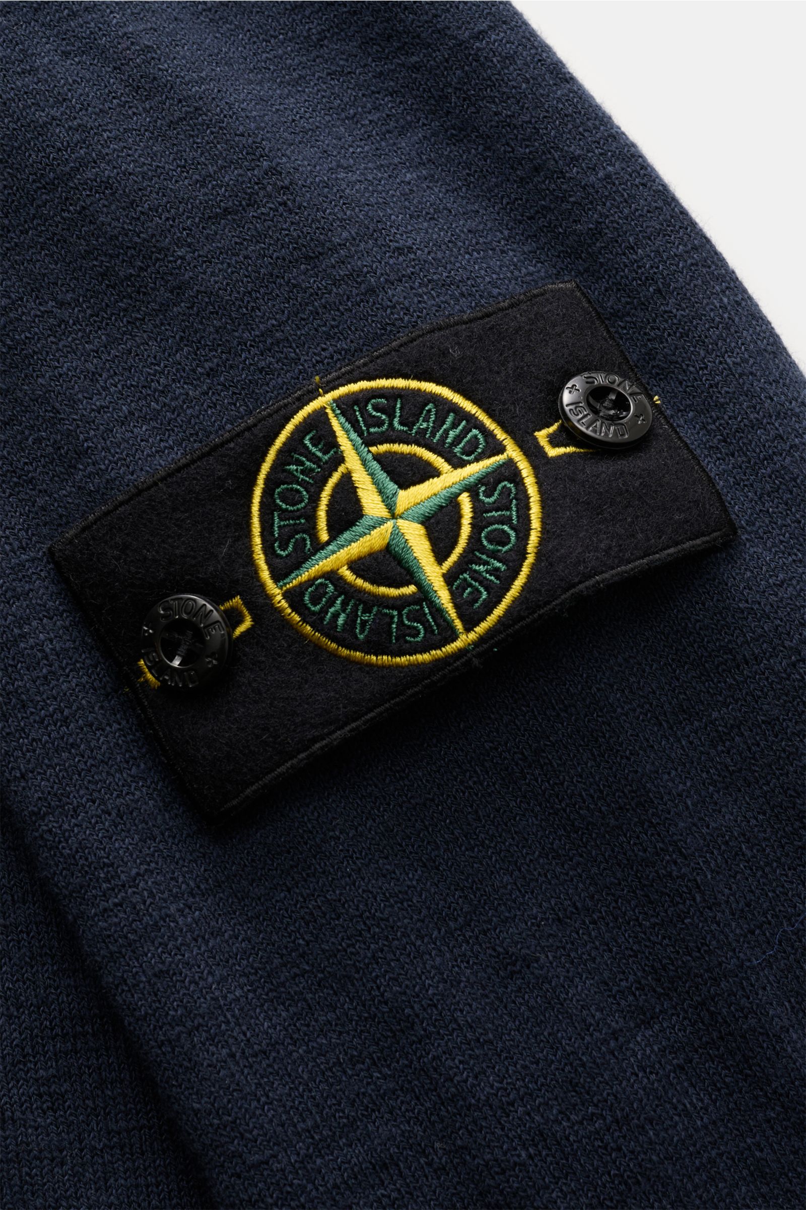 Nahaufnahme des Stone Island Rundhalspullovers navy, Fokus auf das typische Kompass-Badge, feines Strickbild, weicher Griff, Baumwoll-Microfaser-Mix, rollierte Saumkanten und gezielte Nähte sichtbar.
