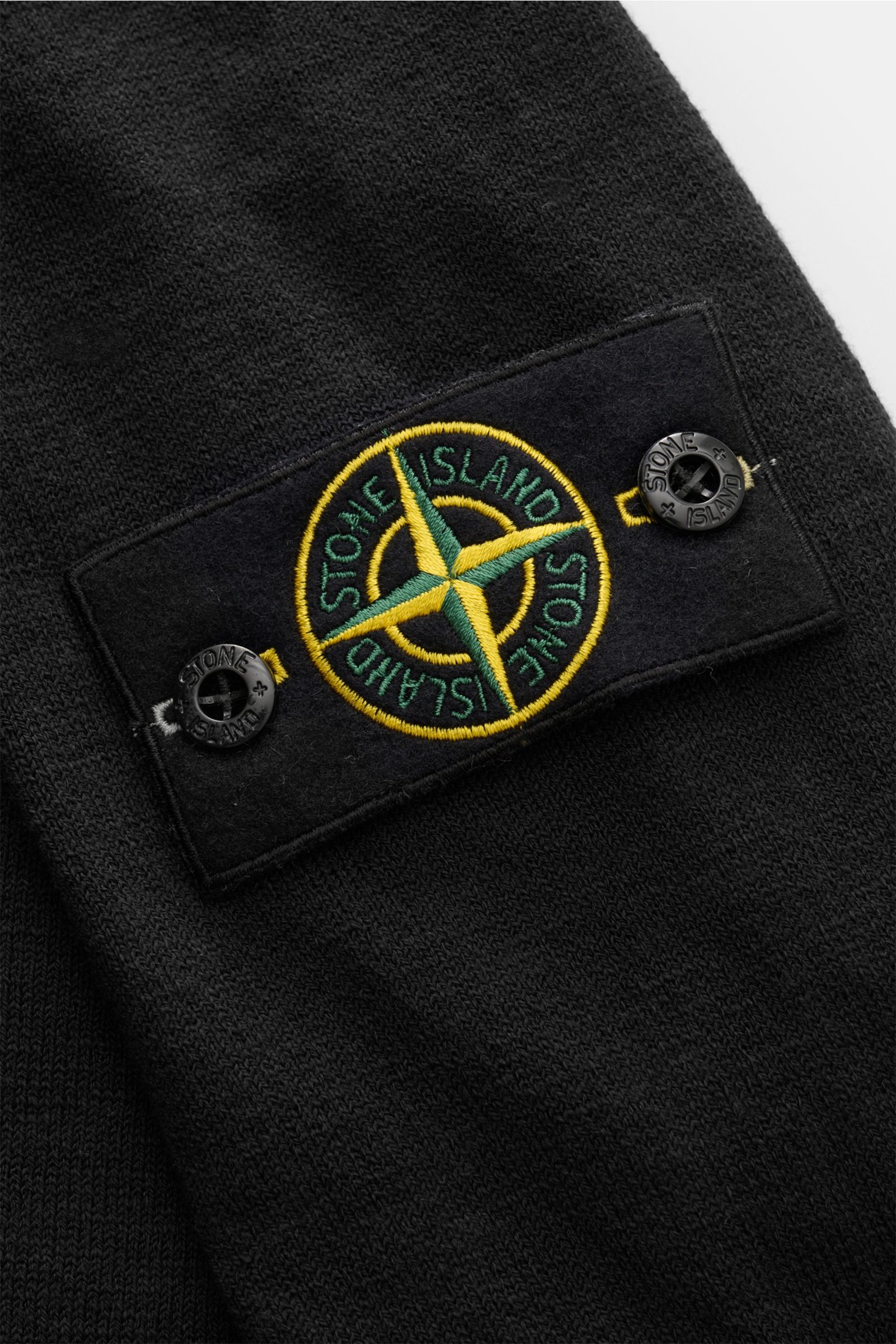 Stone Island Rundhalspullover schwarz in Nahaufnahme, feines Strickbild, rollierte Saumkanten, typisches Kompass-Badge frontal sichtbar.