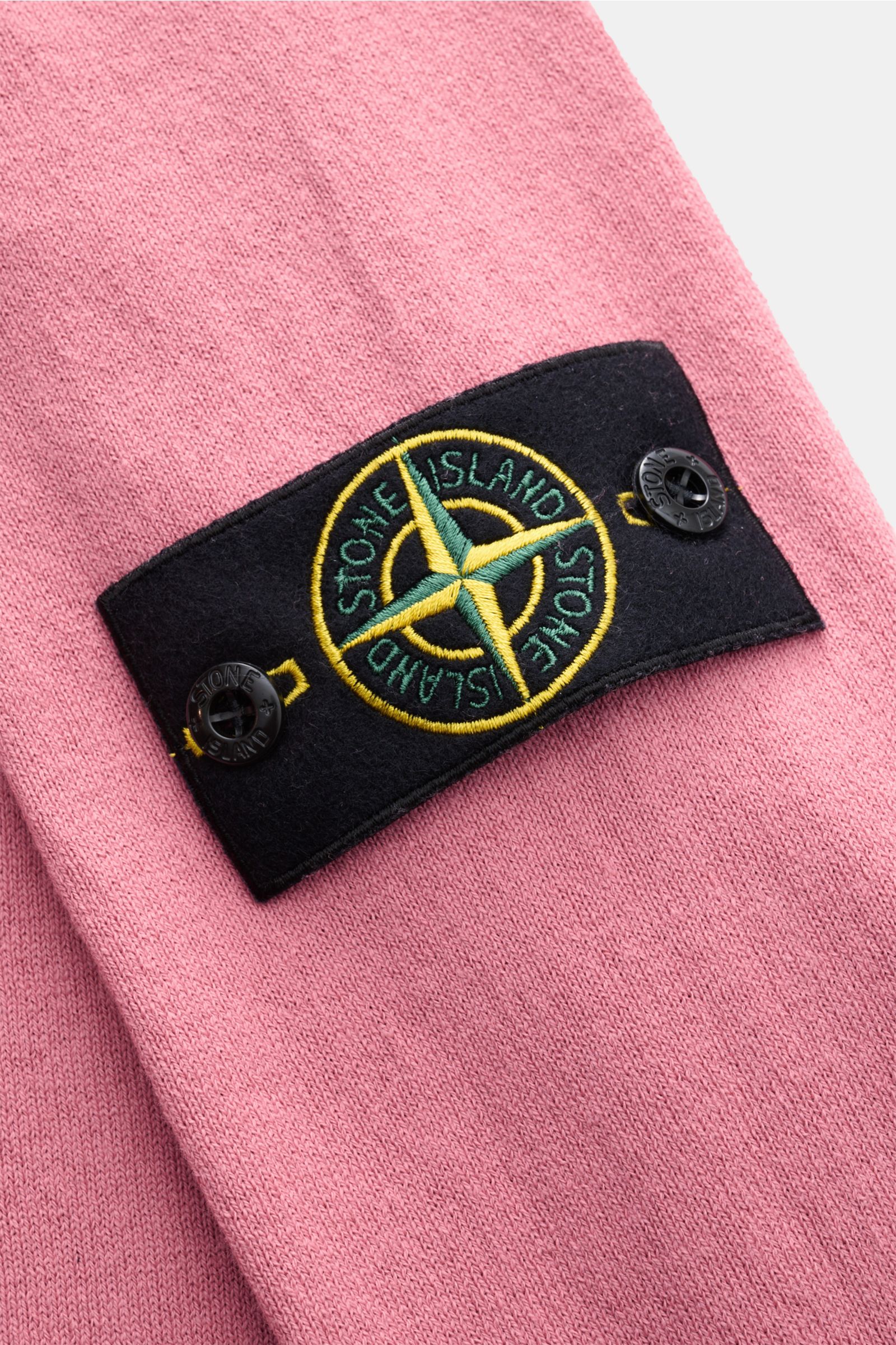 Nahaufnahme des Stone Island Rundhalspullover altrosa mit feinem Strickbild, rollierten Saumkanten und typischem Kompass-Badge aus reiner Baumwolle.
