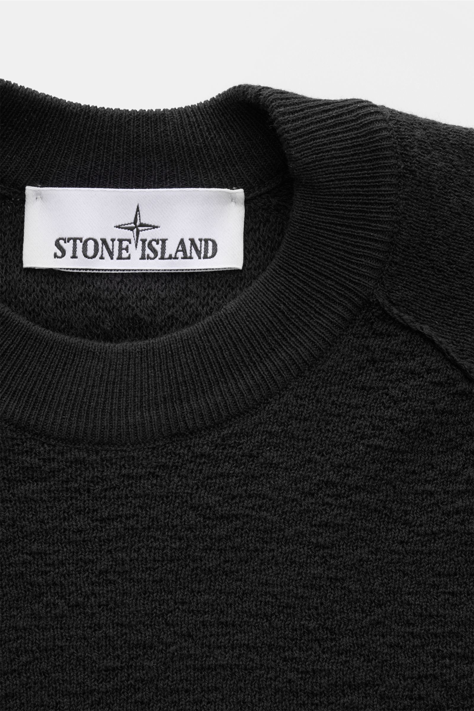 Stone Island Rundhalspullover schwarz, sportiver Strickpullover aus leichter Baumwolle, crincle-Optik, Raglanärmel, Rippbündchen, Detailaufnahme von oben.