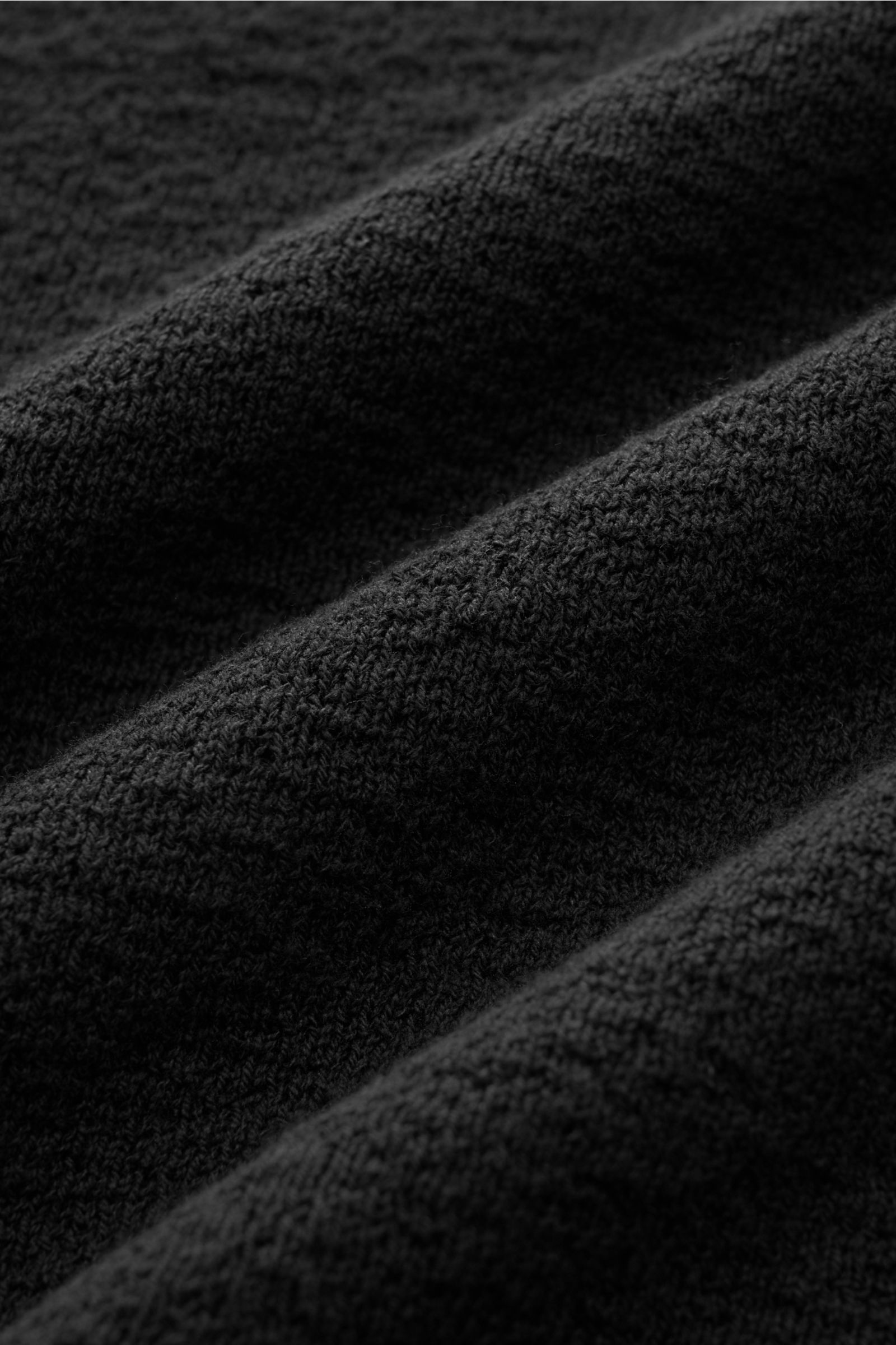 Stone Island Rundhalspullover schwarz aus leichtem Strick, Baumwolle, crincle-Optik, Raglanärmel, Rippbündchen, Logo-Badge, Nahaufnahme Stoffstruktur.