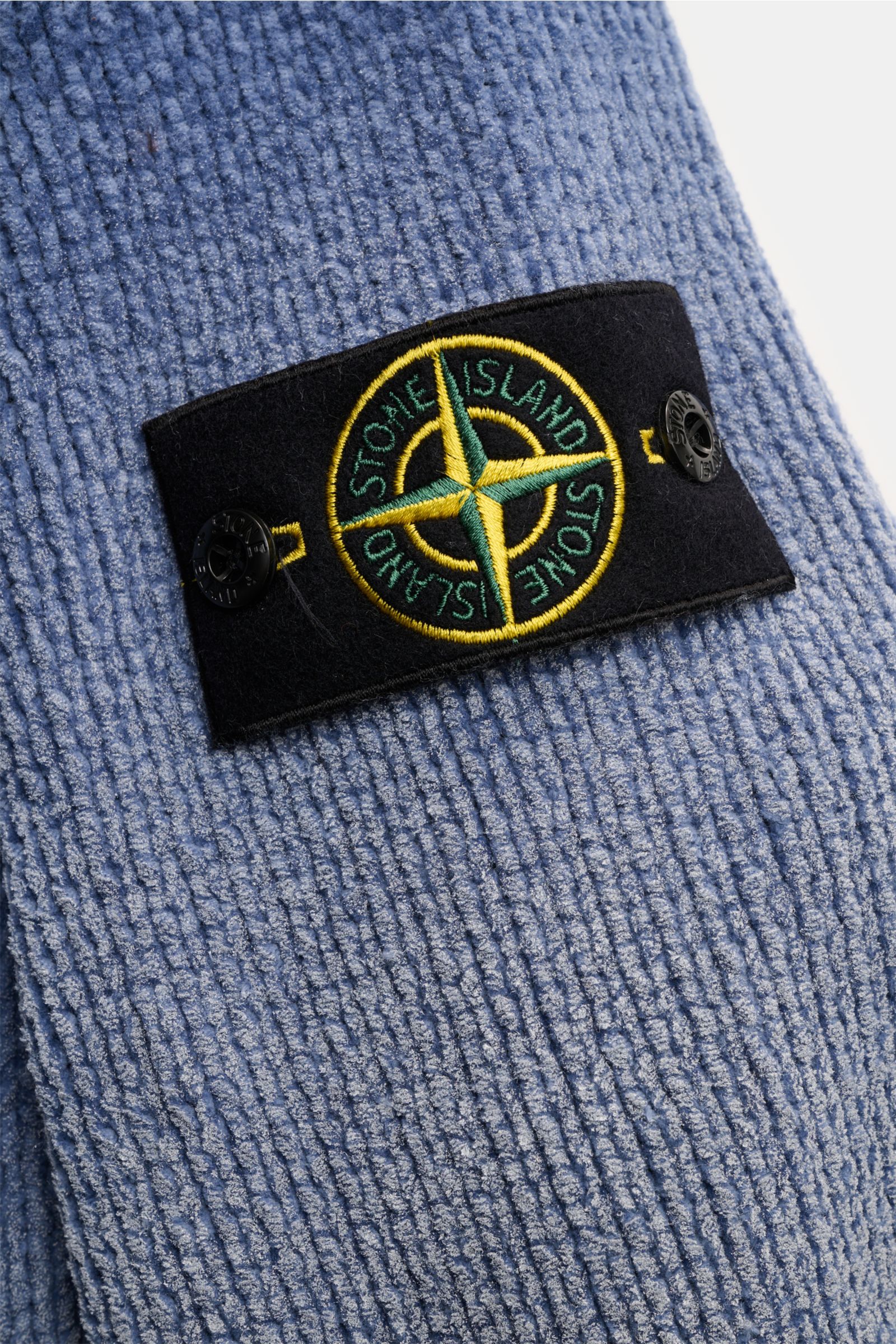 Close-up angled view of the Stone Island Mock Neck Pullover 'Sprayed Chenille' rauchblau showing its textured, medium-knit blue chenille fabric with a spray effect and the black compass badge on the upper arm.

Strick-Highlight: Der STONE ISLAND Chenil