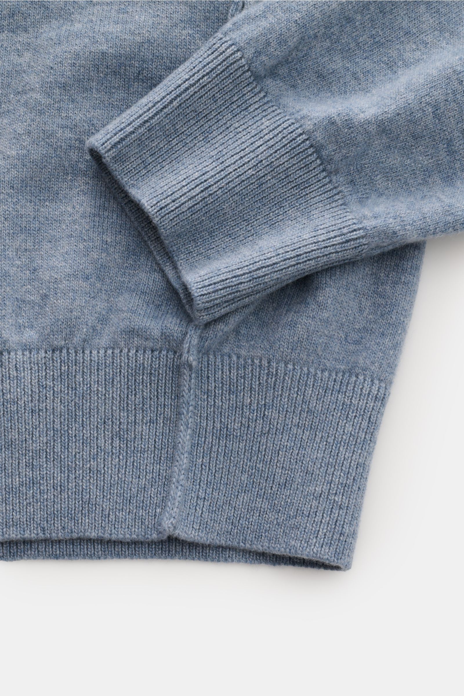 Stone Island Rundhalspullover rauchblau aus reiner Wolle, feines Strickbild, elastische Rippbündchen, tonales Kompass-Badge, Detailaufnahme von Ärmel und Saum.