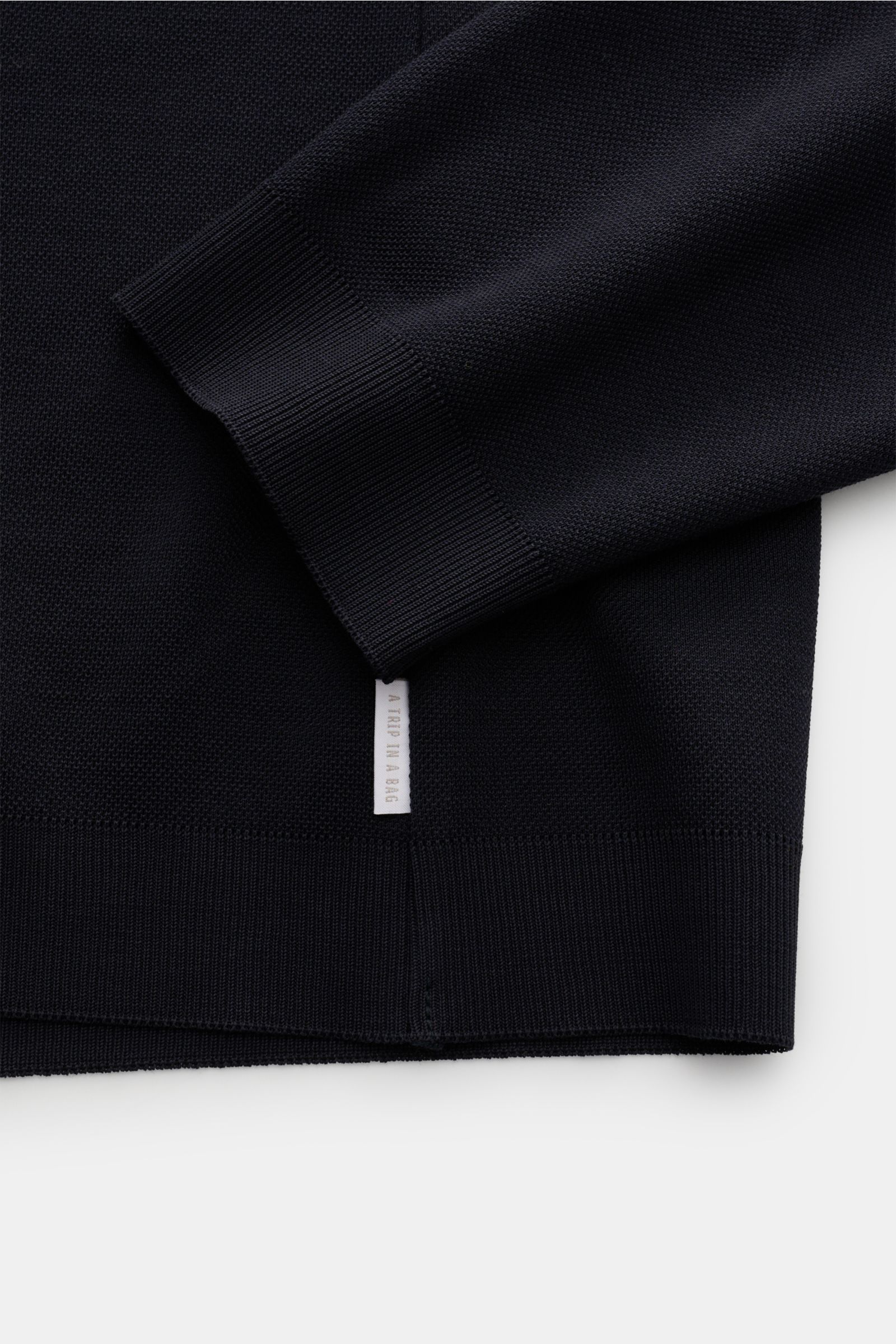 Close-up image of the sleeve and hem of the 04651/ A trip in a bag Rundhals-Longsleeve 'If Tee' navy, photographed from above, showing the elastic cotton jersey fabric, ribbed cuffs, and a small white woven label in the side seam. Das unkomplizierte 'I
