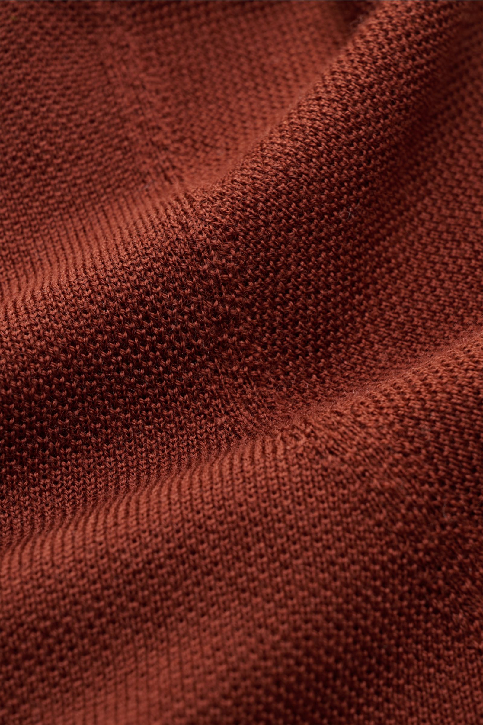 Close-up image of finely knitted fabric in a warm rust color, showing texture and weave details from an angled perspective. The 04651/ A trip in a bag Feinstrick-Rundhalspullover dunkelblau meliert is a timeless classic for autumn and winter, made from pu