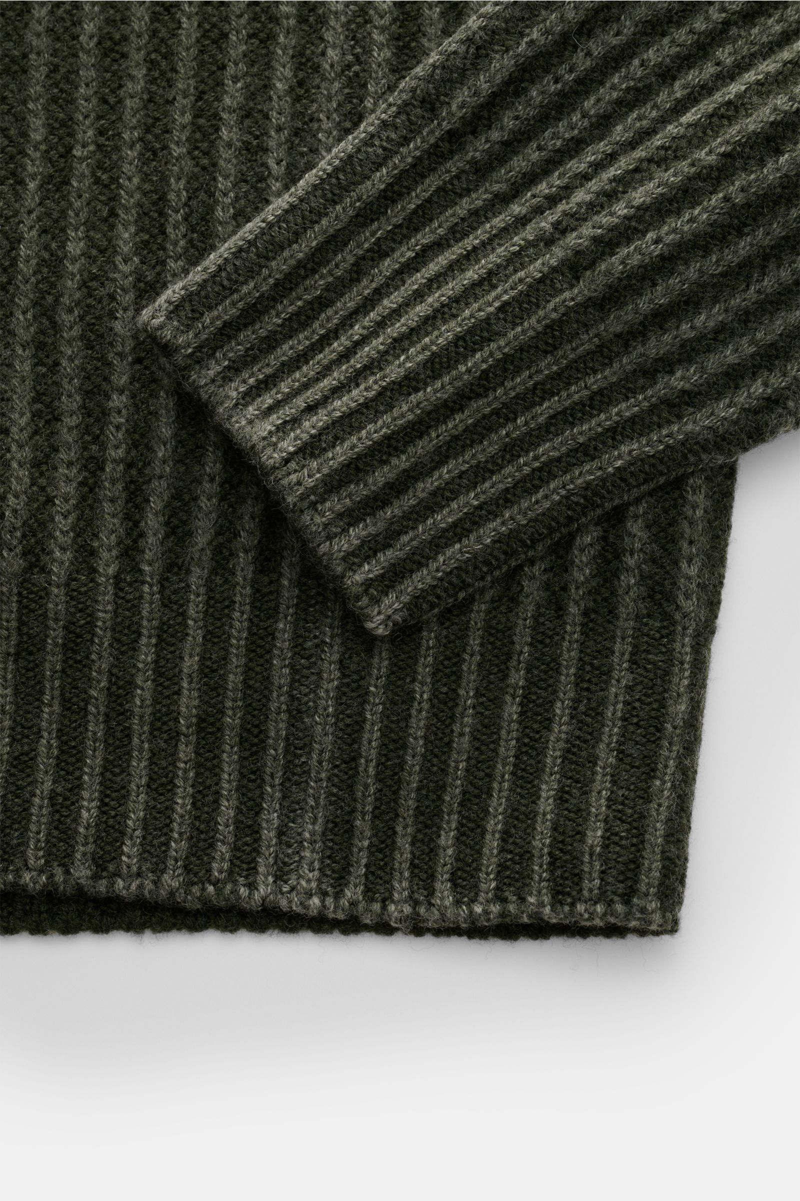 Close-up view of the ribbed sleeve and hem of the 04651/ A trip in a bag Mock Neck Pullover 'Foggy Mock' dunkelgrün, showing its grobes Rippstrickmuster and soft wool texture. Hochwertiger Tragekomfort mit lässigem Stil – der vielseitig kombinierbare Stri