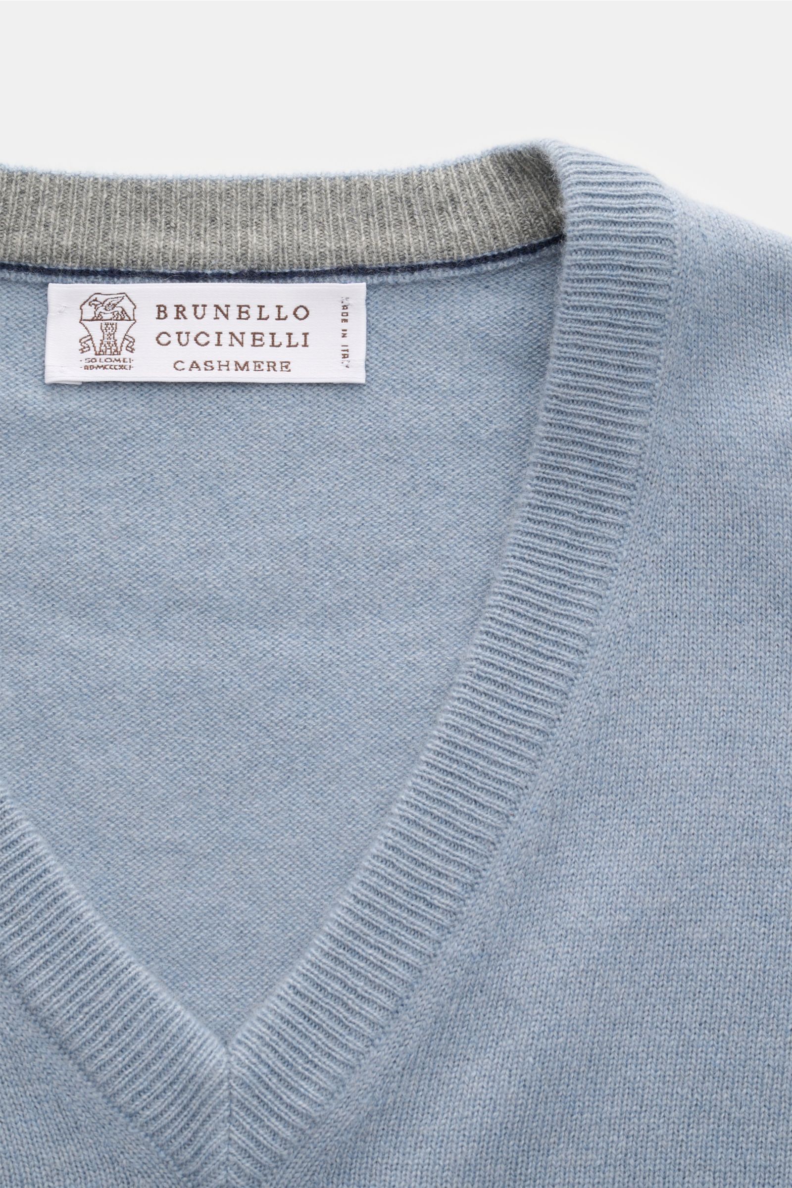 Nahaufnahme des rauchblauen Brunello Cucinelli Cashmere V-Neck Pullovers mit feinem Strickbild, schmalen Kontrastkanten und V-Ausschnitt.