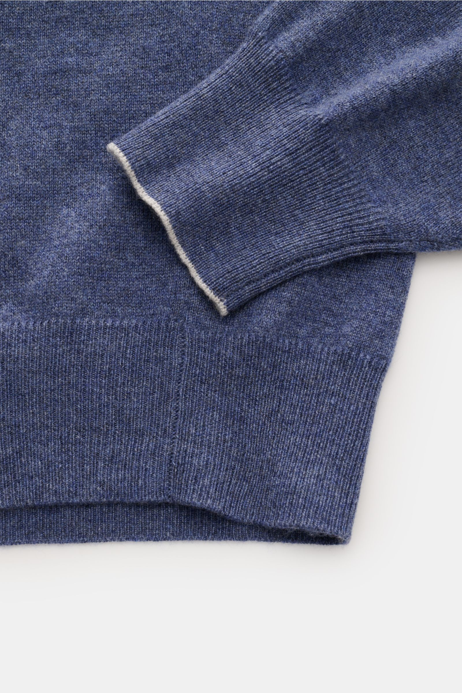 Brunello Cucinelli Cashmere V-Neck Pullover blau meliert shown in close-up from above, highlighting fine knit, soft texture, ribbed cuffs, slim contrast edges, and regular fit.  
Luxuriöser Cashmere in Verbindung mit klassischem Design: Der V-Neck Pull