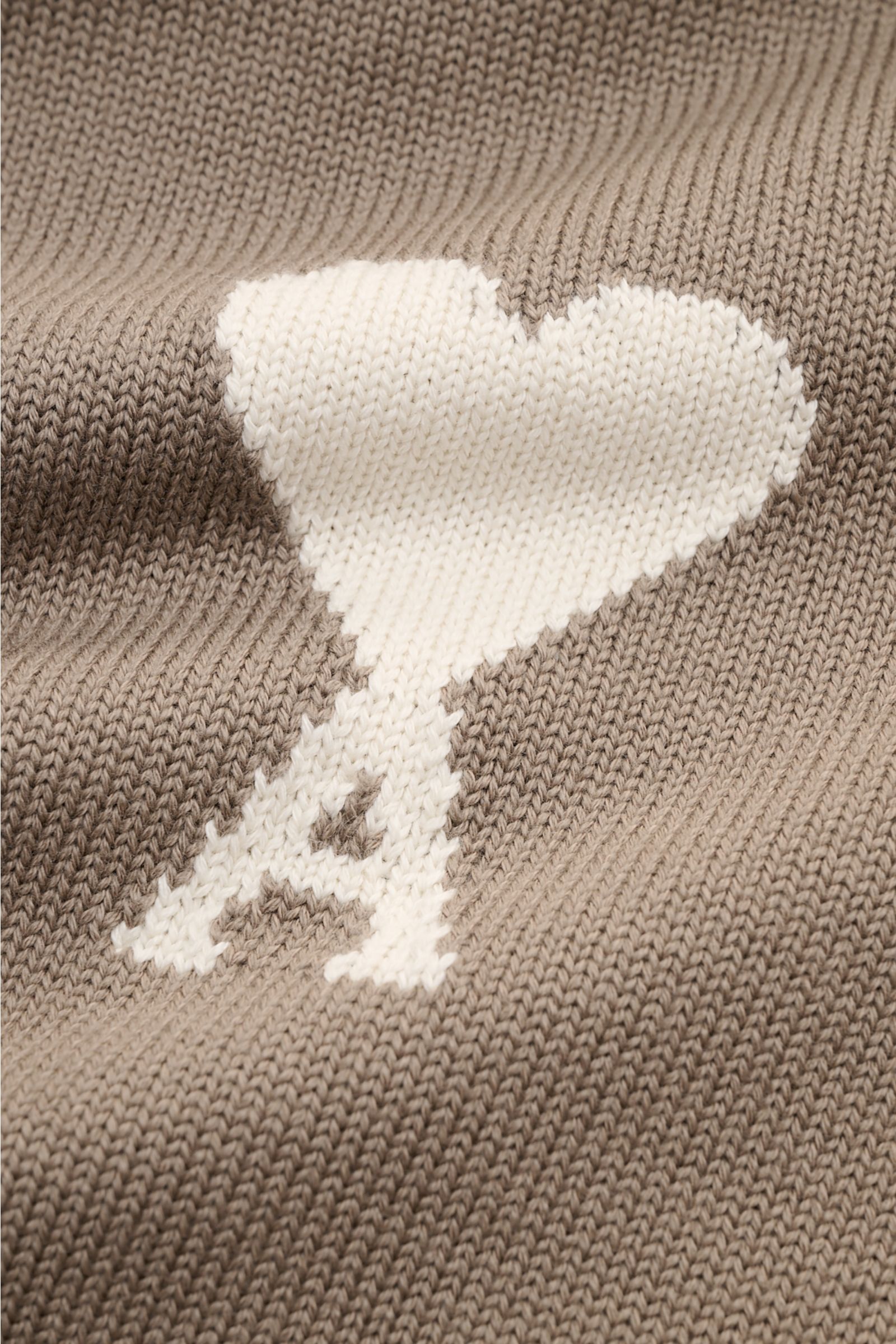 Nahaufnahme des eingestrickten weißen Logos auf der Brust des Ami Paris Rundhalspullover 'ADC' graubraun mit weichem, mittelfeinem Strickbild.